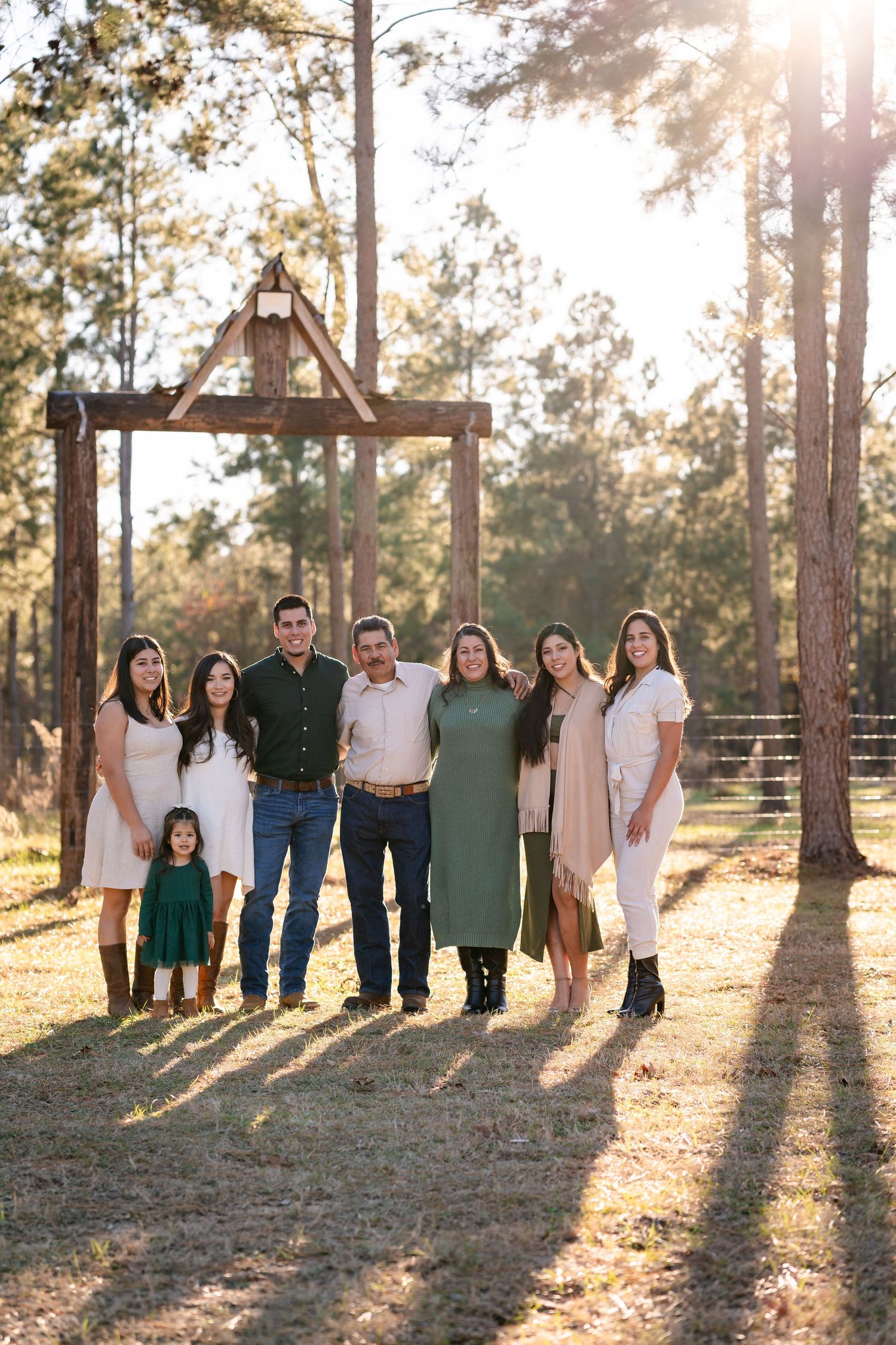 A group portrait under a rustic wooden arch frame in a sunlit forest setting.