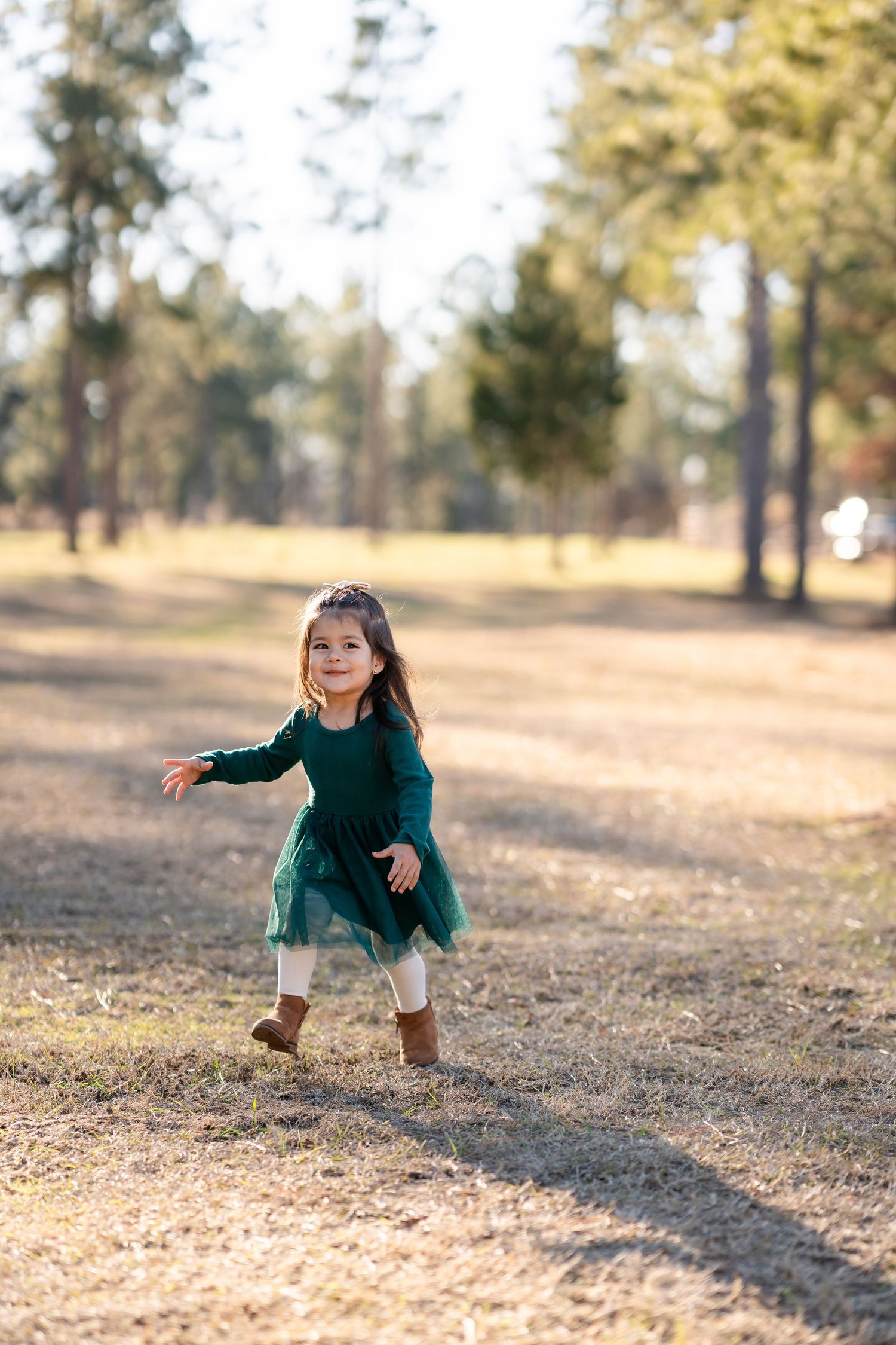 Little one in emerald dress playing energetically in a sunlit outdoor setting.