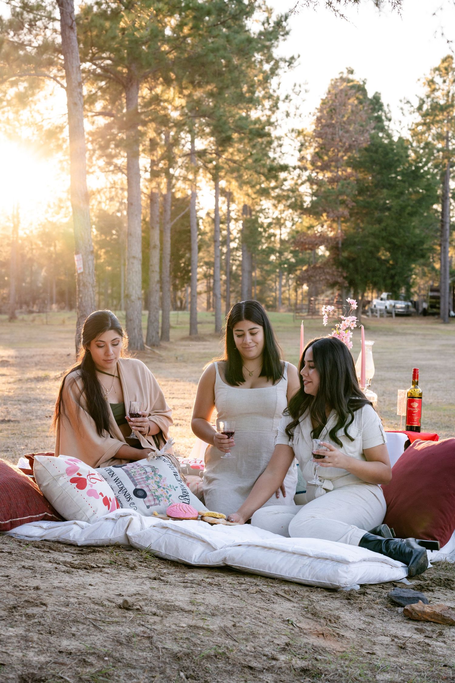 Three friends relaxing on blankets during sunset picnic in forest setting.