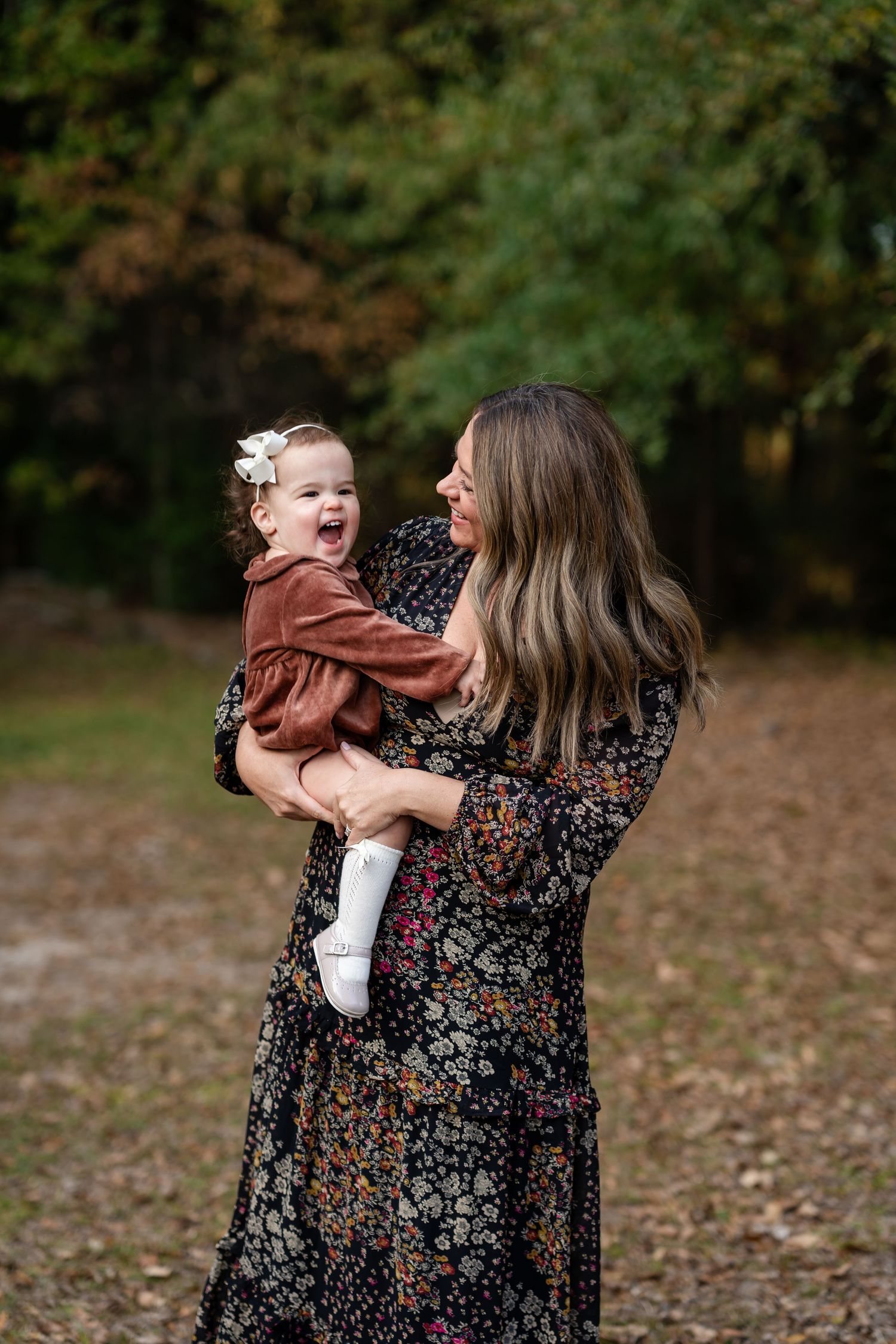 Mother and toddler share playful moments together among autumn leaves and trees.