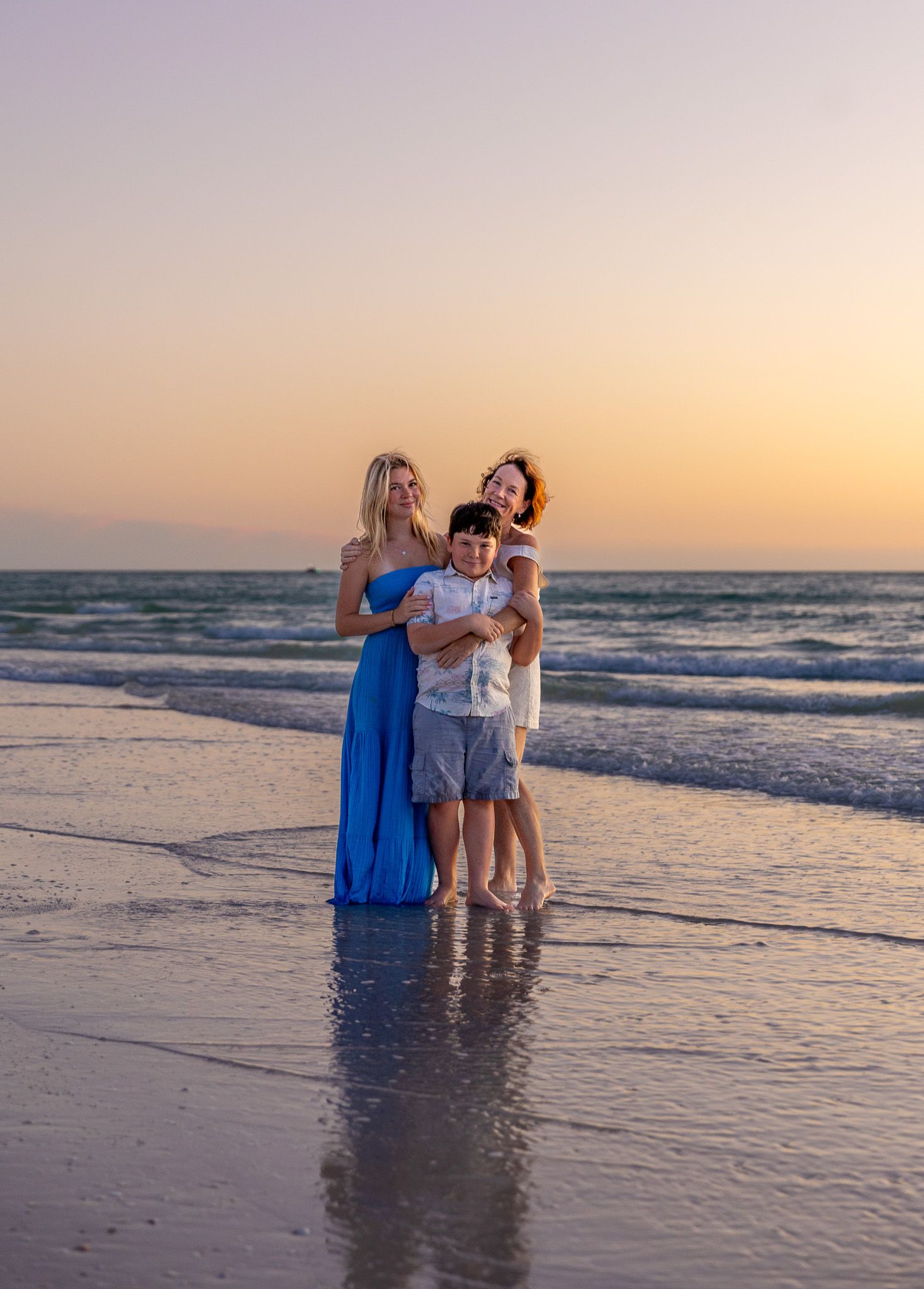 Three people share a joyful moment together at sunset on a beach with gentle waves in the background.