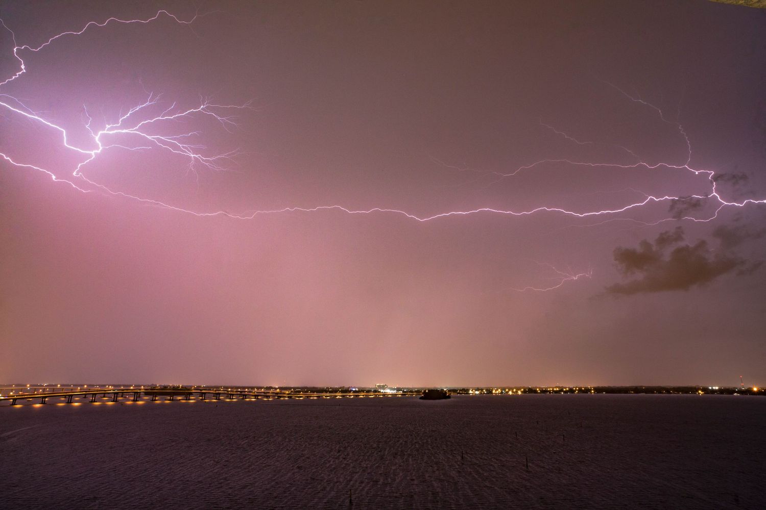 Purple lightning storm illuminates the night sky over a distant city skyline.