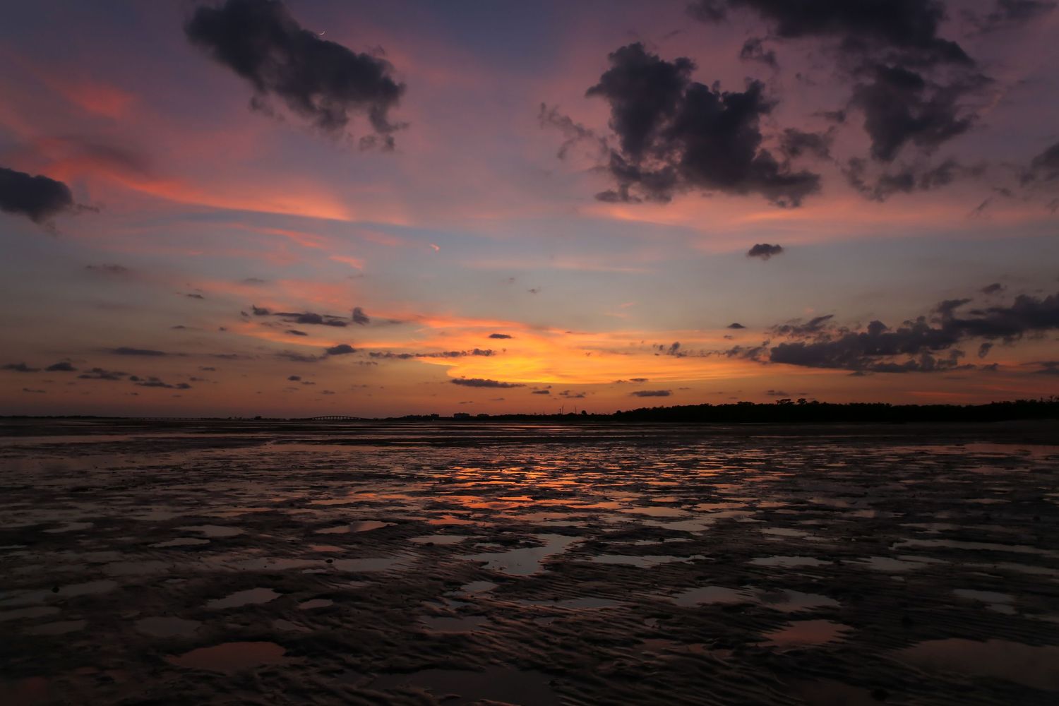 Dramatic sunset over a dark rippling ocean with vibrant orange and pink clouds reflecting on the water's surface.