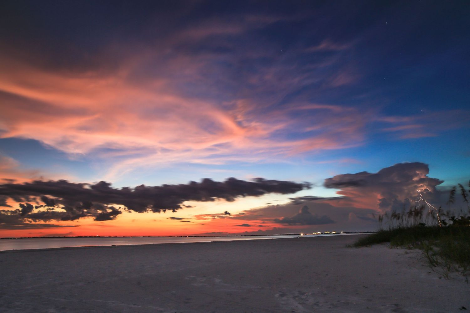 Panoramic view of a dramatic sunset sky with vibrant orange clouds reflecting over a beach shoreline.