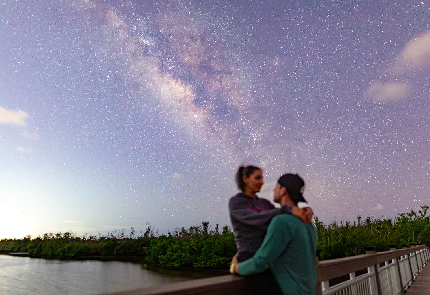 Two people stand silhouetted against a starry night sky with the Milky Way galaxy visible in the background.