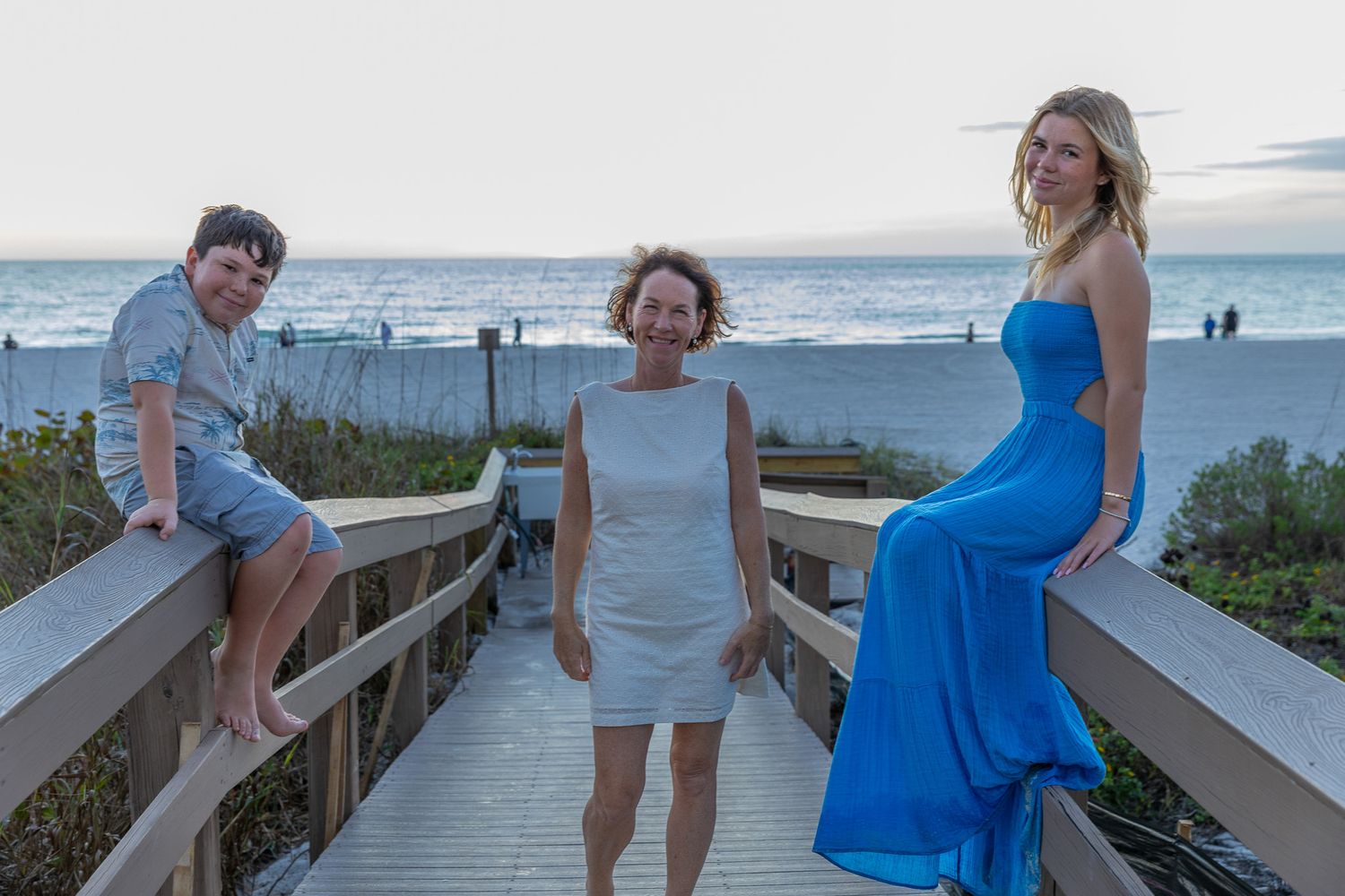 A group of people enjoying a sunny day on a wooden boardwalk leading to the beach.