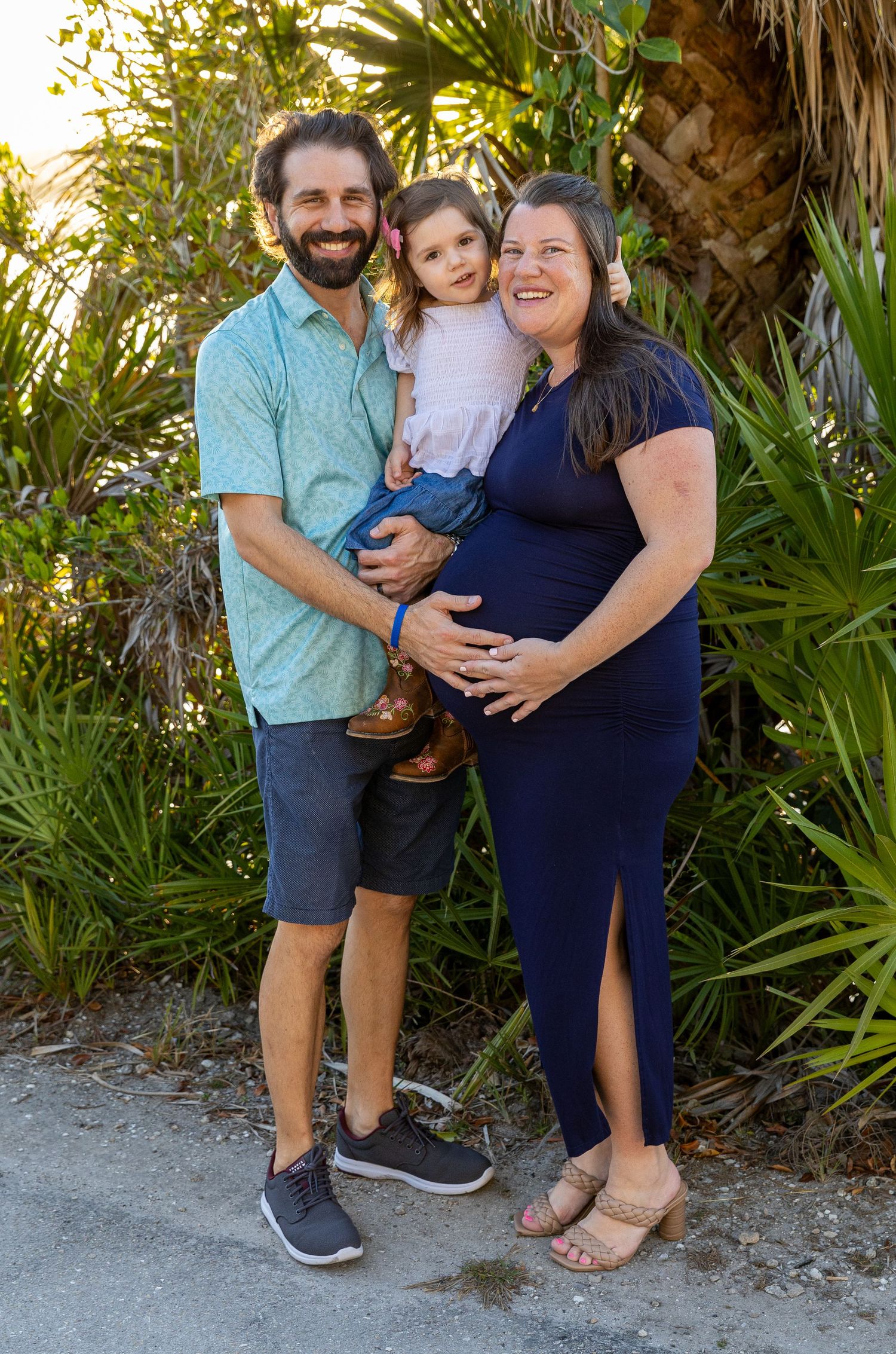 A family poses together against a backdrop of tropical plants and palm fronds in an outdoor setting.