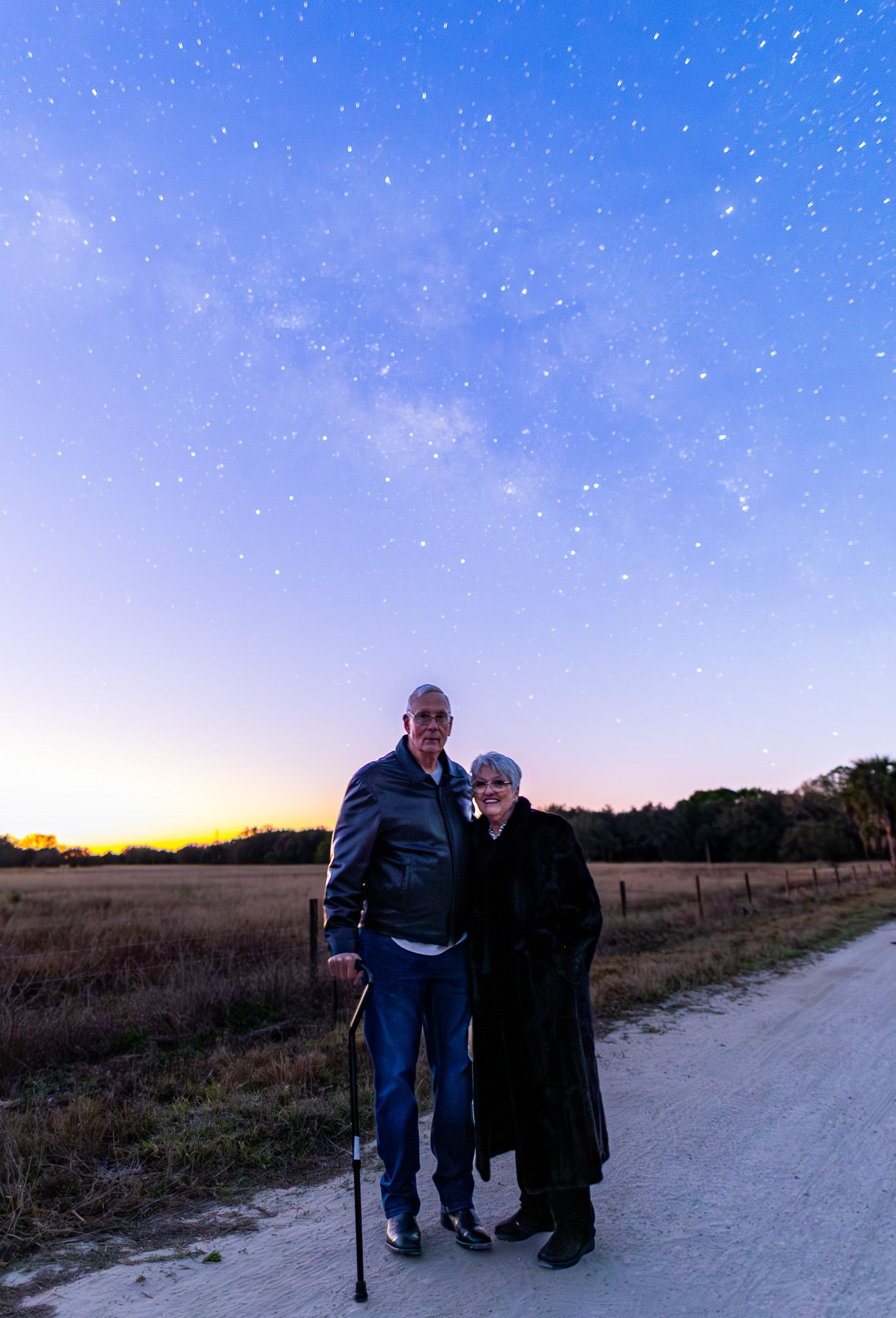 Two people walking together on a dirt path at dusk with a starry sky overhead.