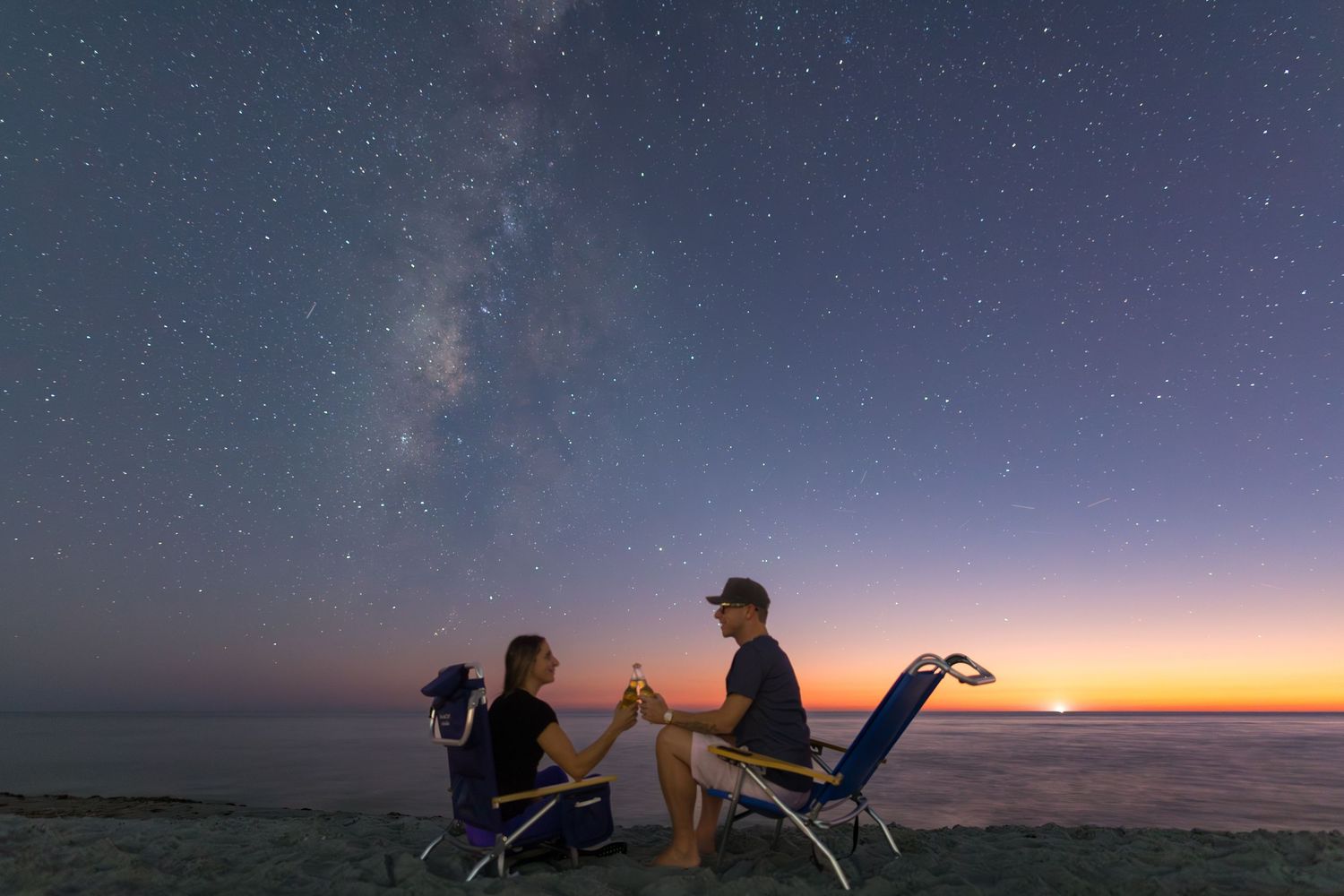 Silhouettes of photographers capturing a vibrant sunset over a serene landscape.
