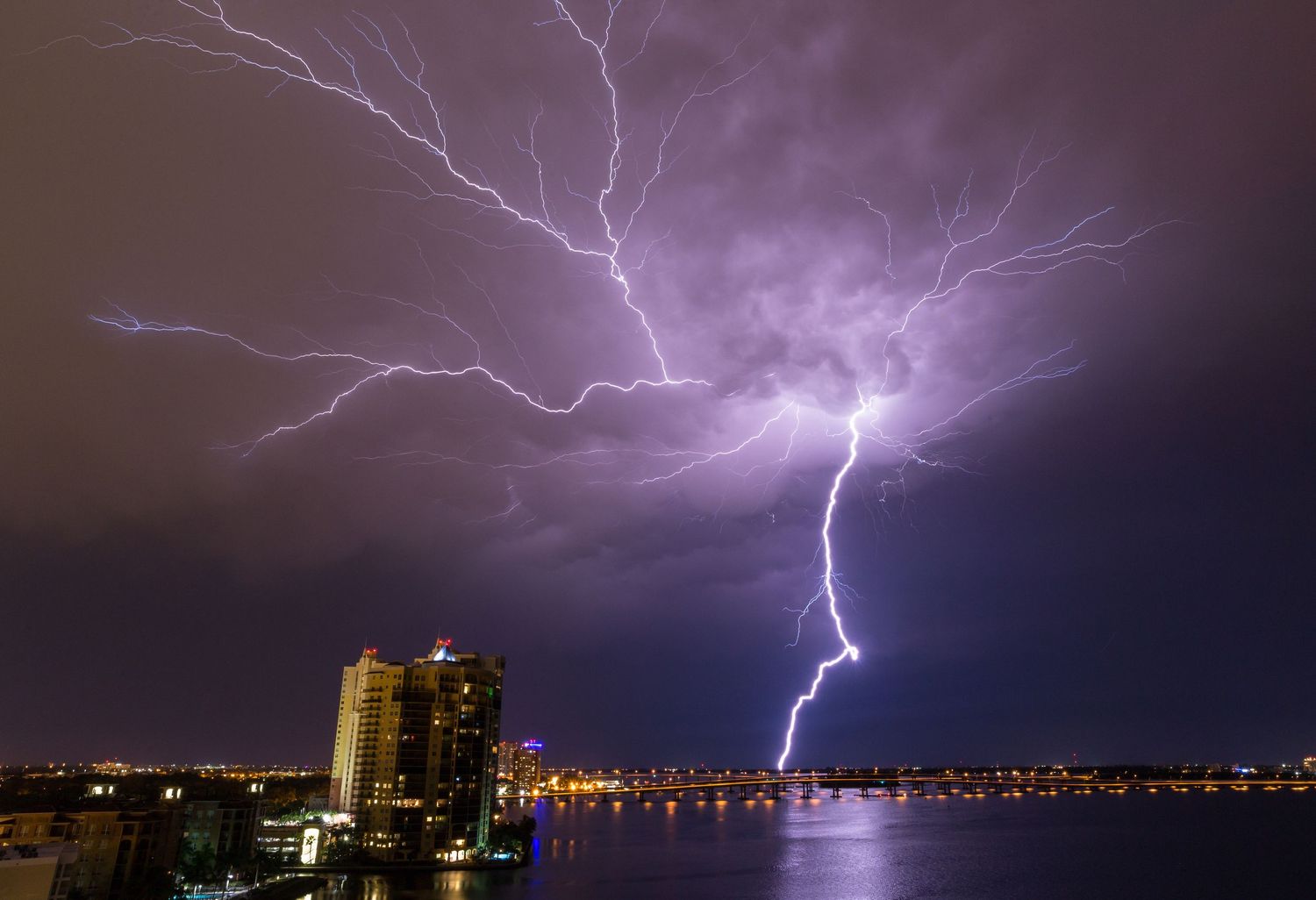 Lightning bolts illuminate the night sky over a city skyline during an intense electrical storm.