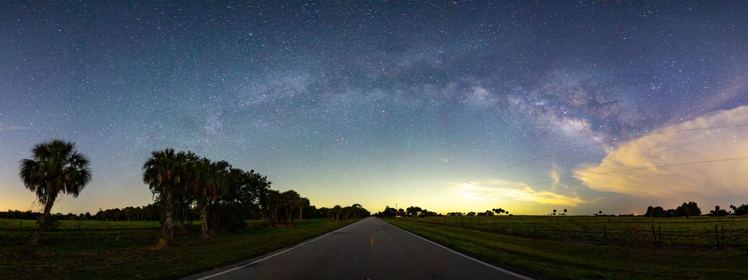 A dramatic panoramic view of a starry night sky over a rural landscape.
