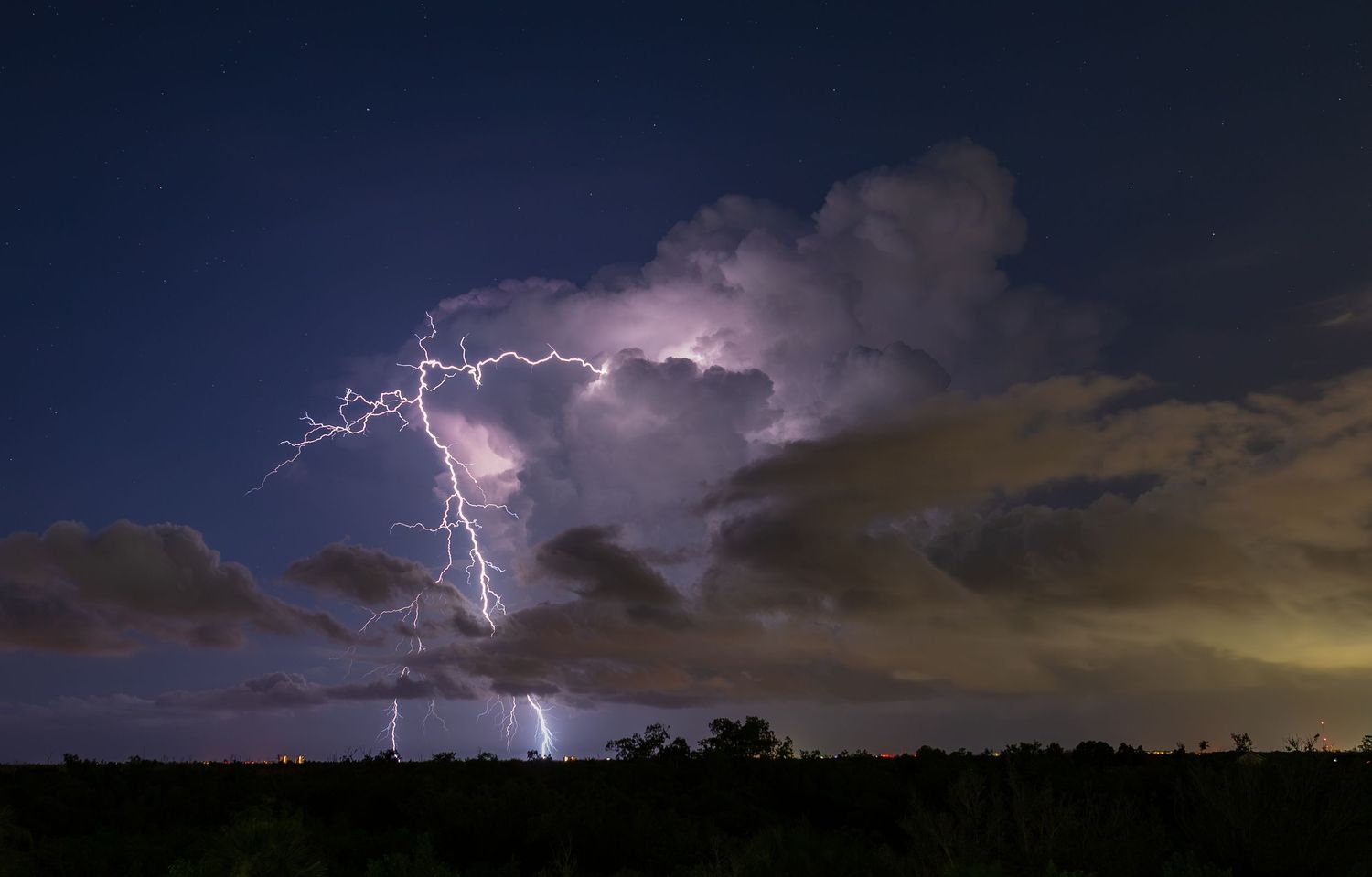 Lightning bolts illuminate a dramatic night sky over a dark rural landscape during a powerful thunderstorm.