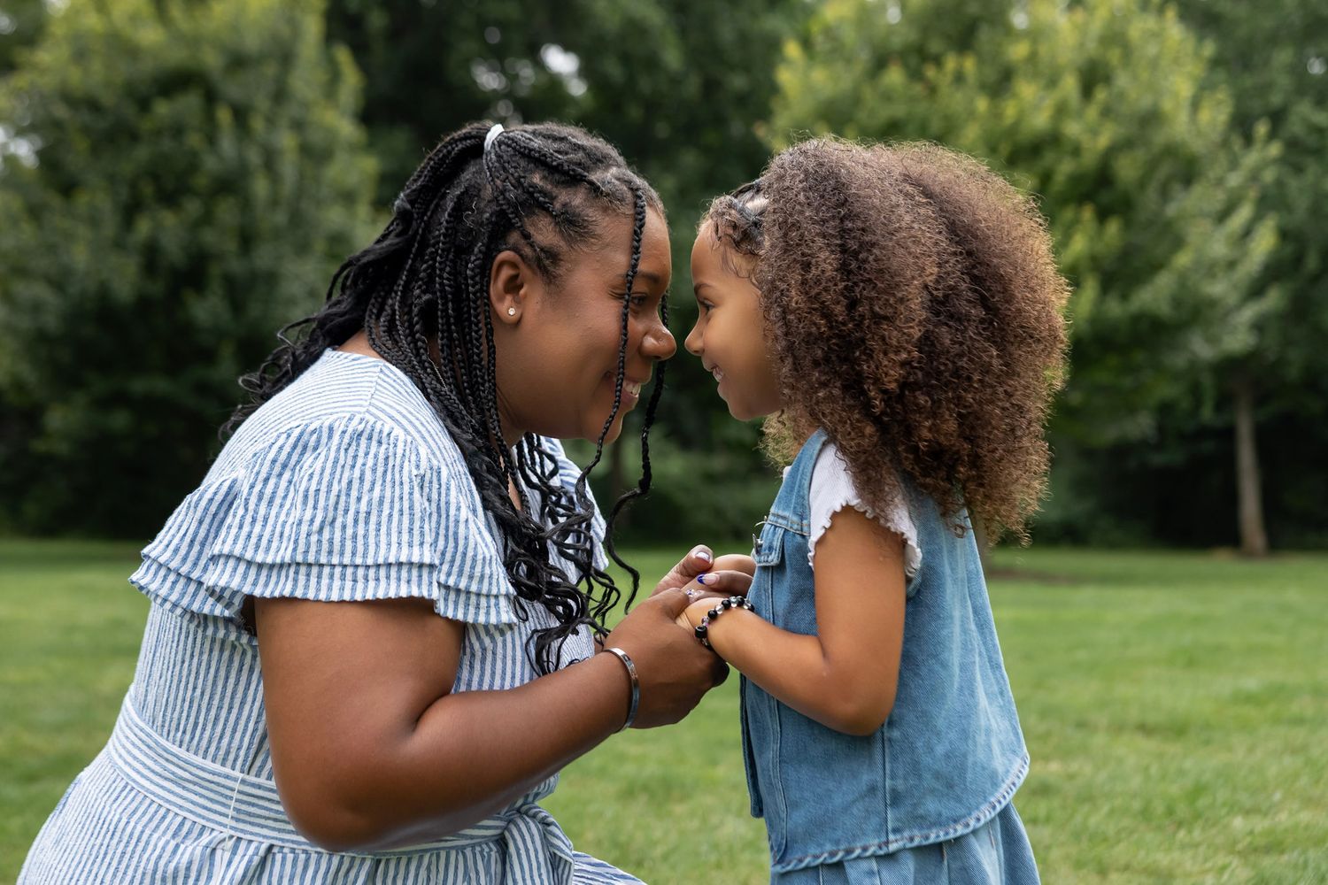 mother and daughter holding hands with their faces pressed together in nature scenery