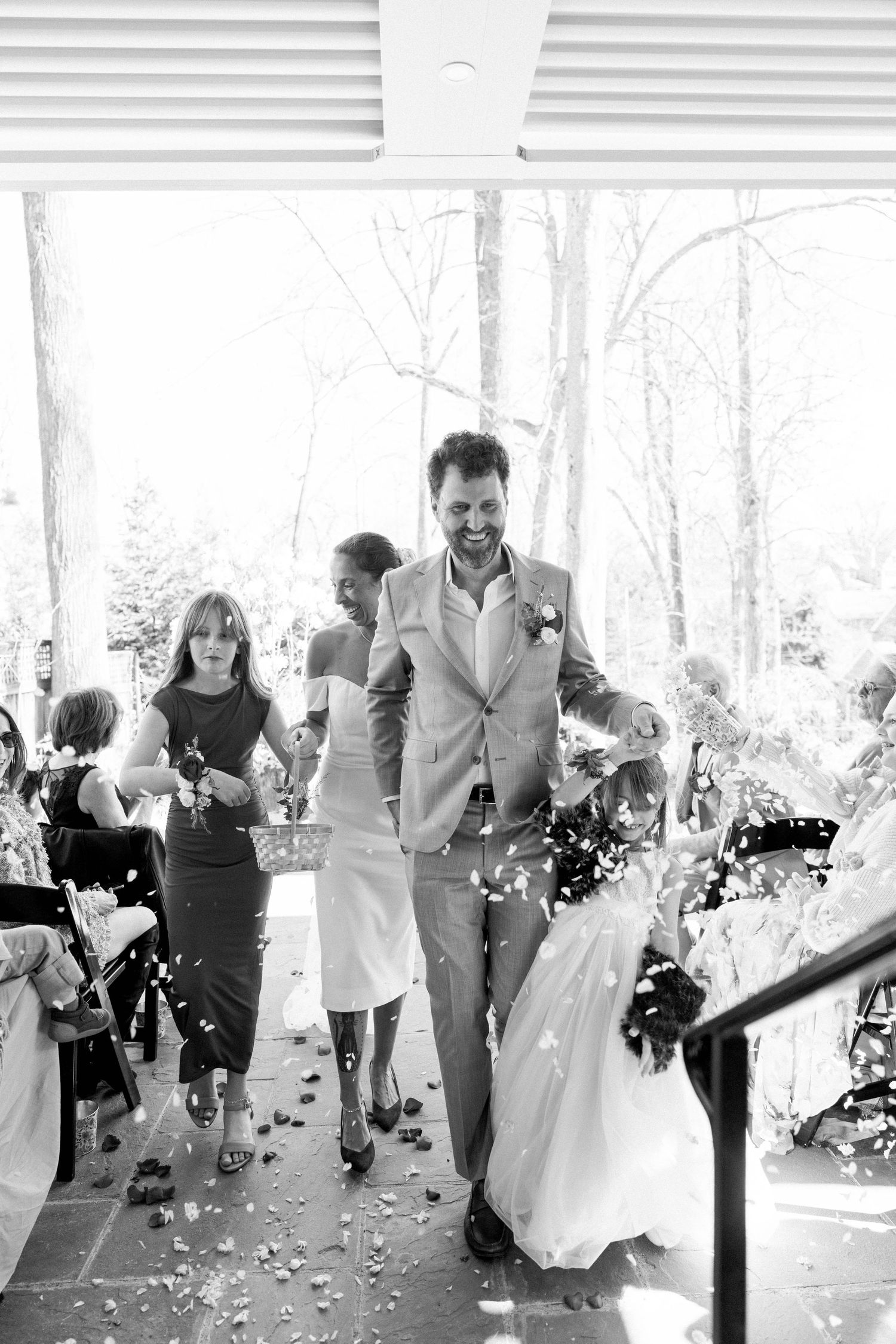 Bride and groom walking with daughters and flower petals.