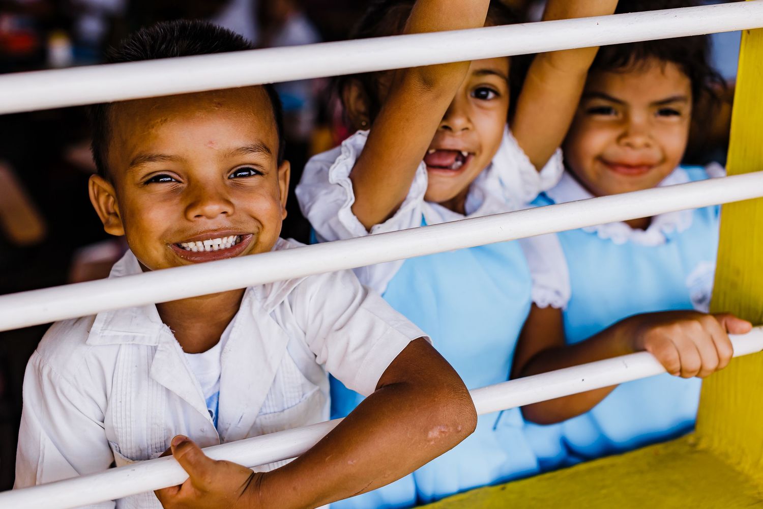 Children peeking through white horizontal bars with bright smiles.
