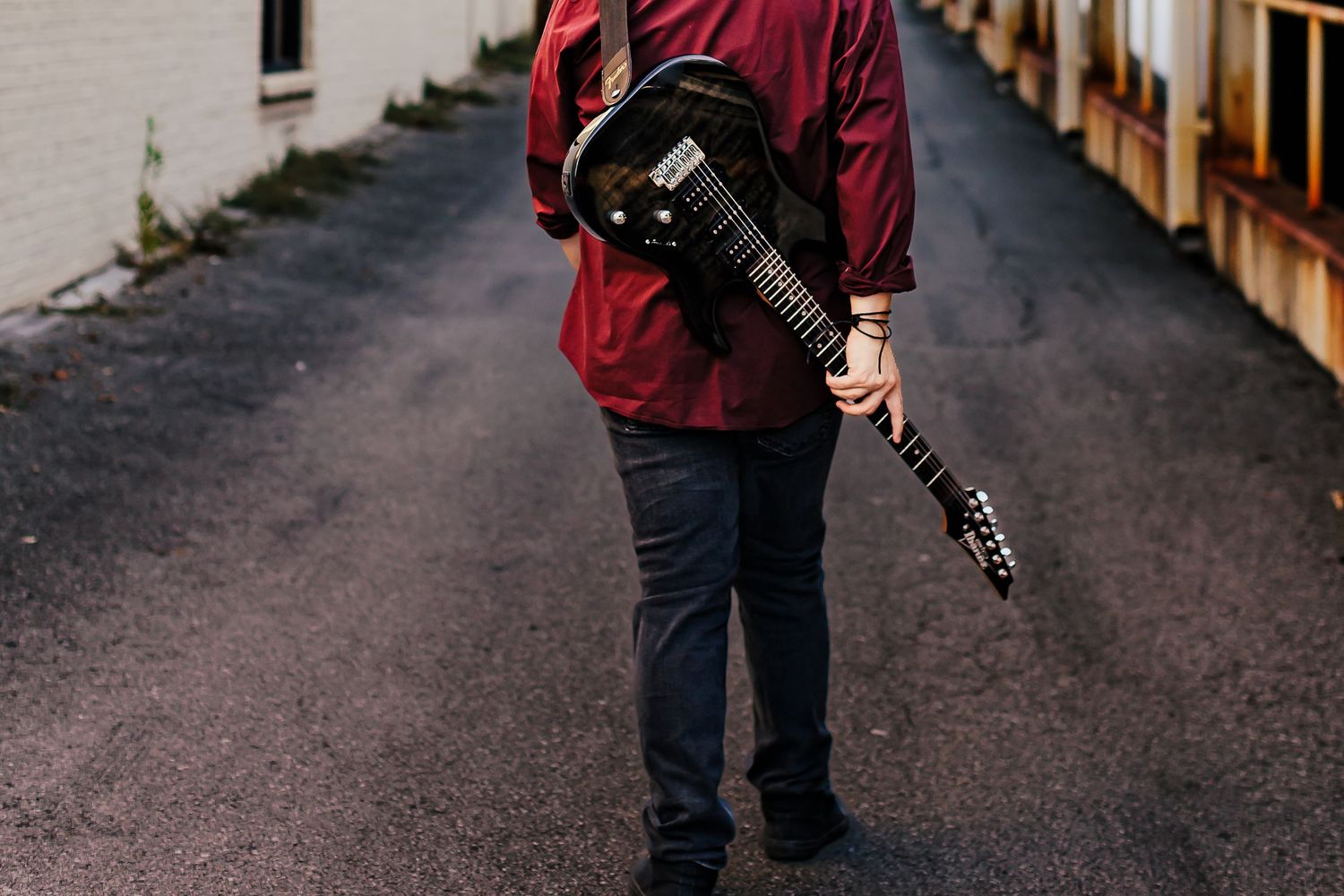 Person holding an acoustic guitar while standing on an asphalt road.