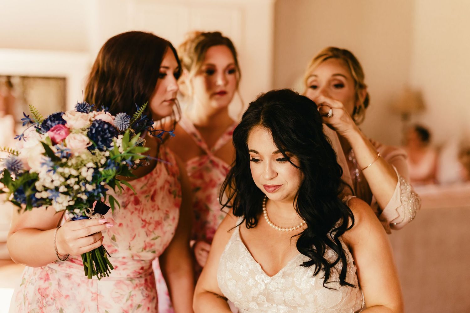 Bridesmaids in pink dresses help with final wedding preparations while holding a colorful floral bouquet.