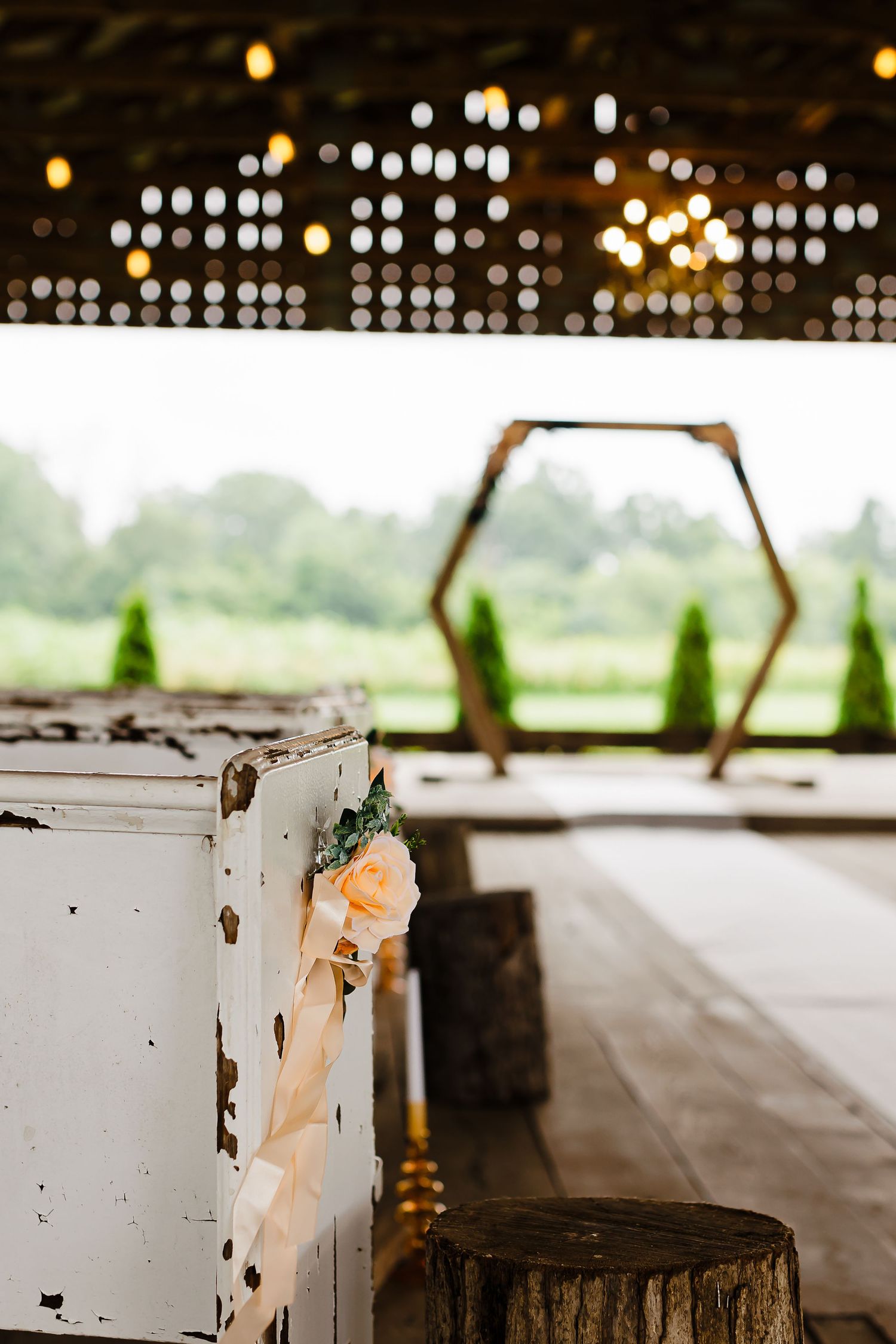 Rustic wedding venue setup with hexagonal arch and vintage white cabinet against a blurred outdoor background.