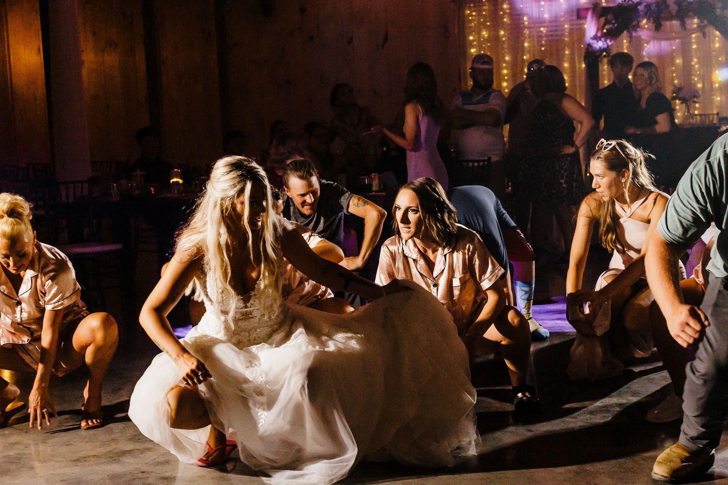 Wedding celebration on rustic barn dance floor with dramatic party lighting.