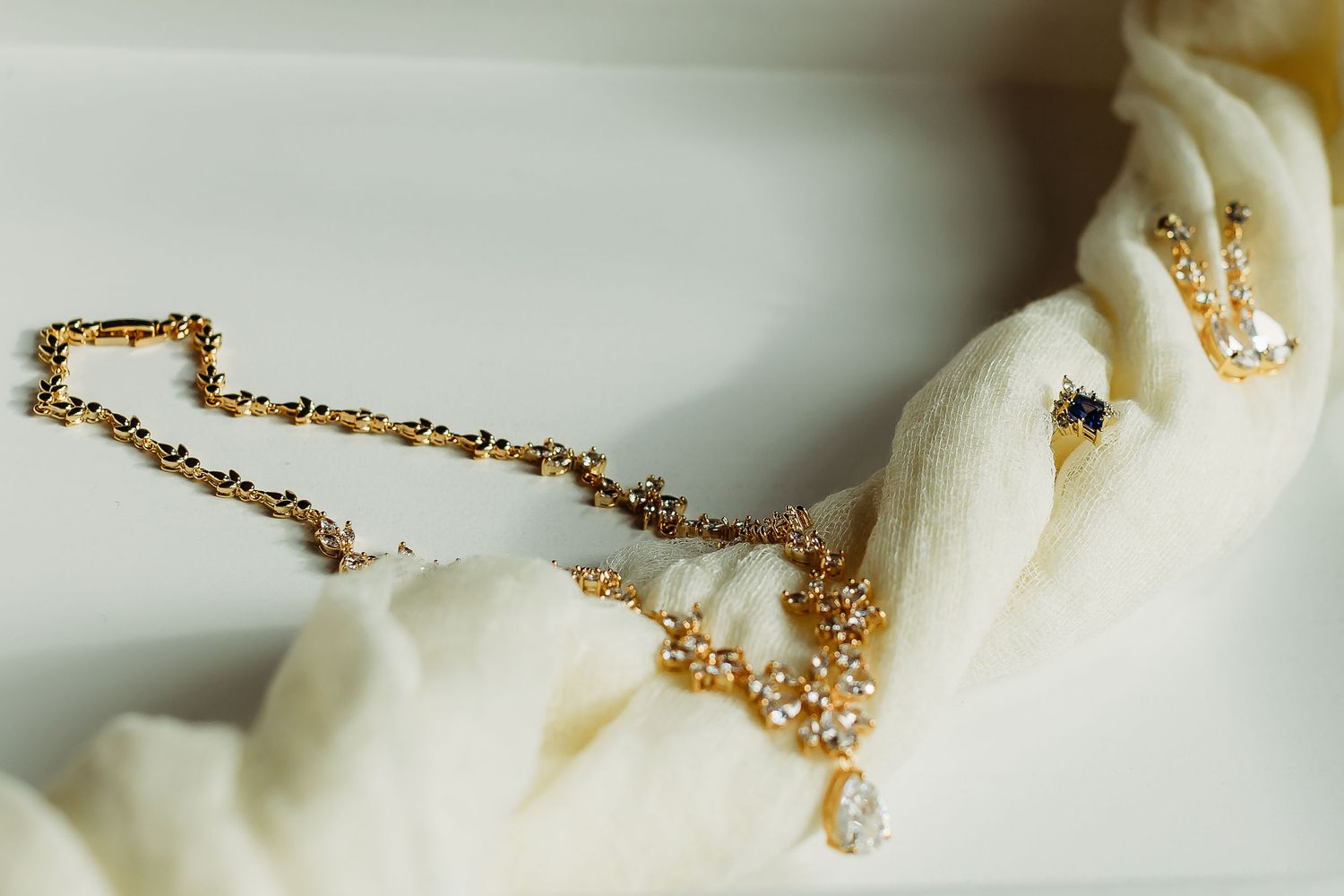 Close-up of delicate gold chain jewelry details on white fabric.