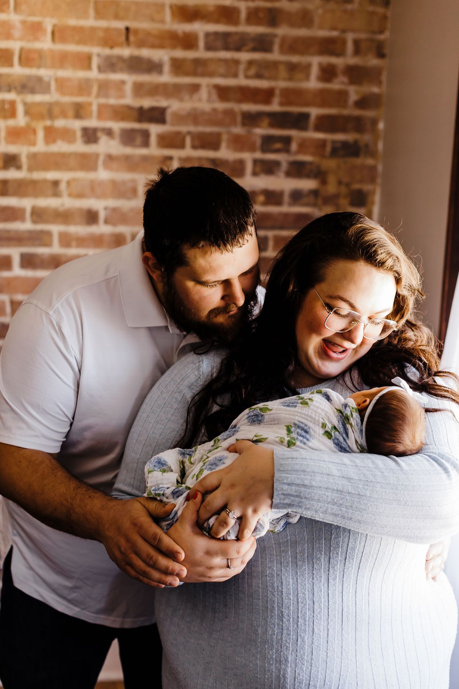 A tender family moment captured against a rustic brick wall background.