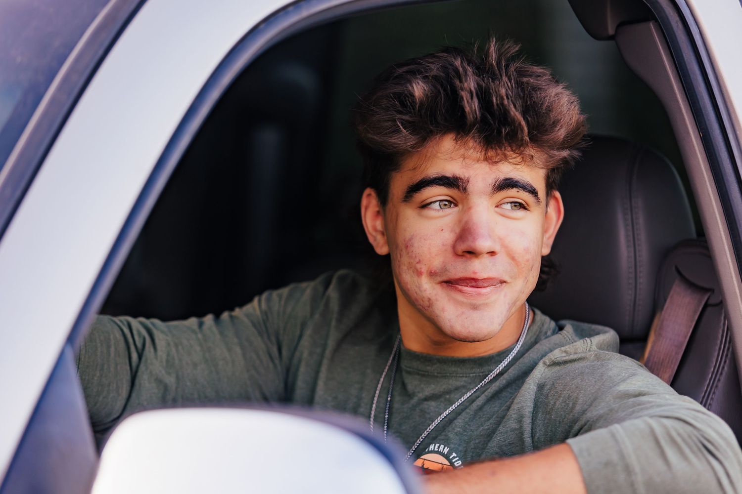Young person smiling while sitting in the driver's seat of a car.