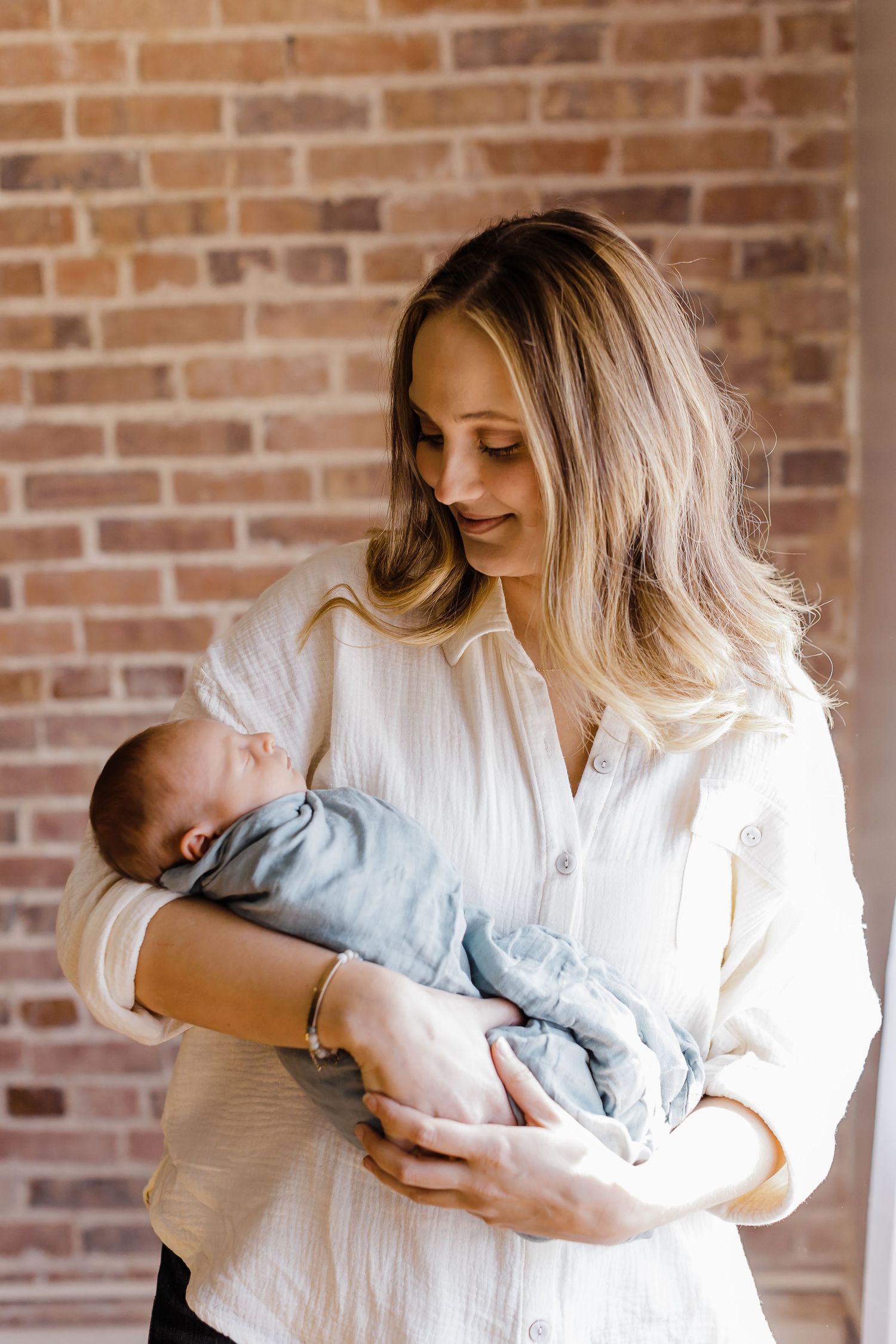 A tender moment between parent and newborn baby against a rustic brick wall.
