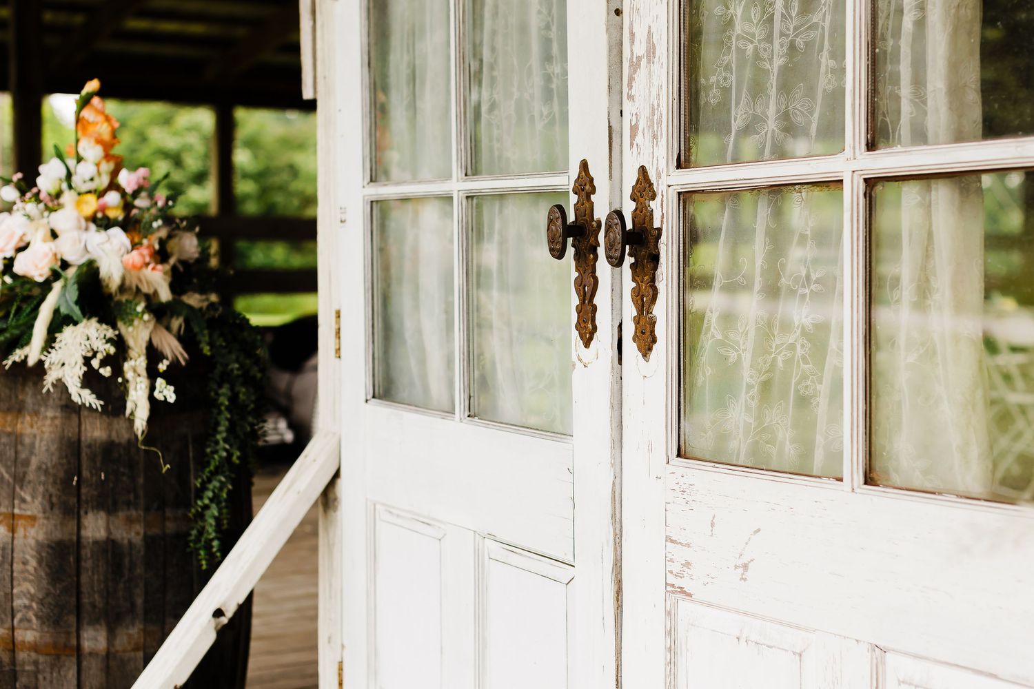 White French doors decorated with floral arrangements at a rustic wedding venue.
