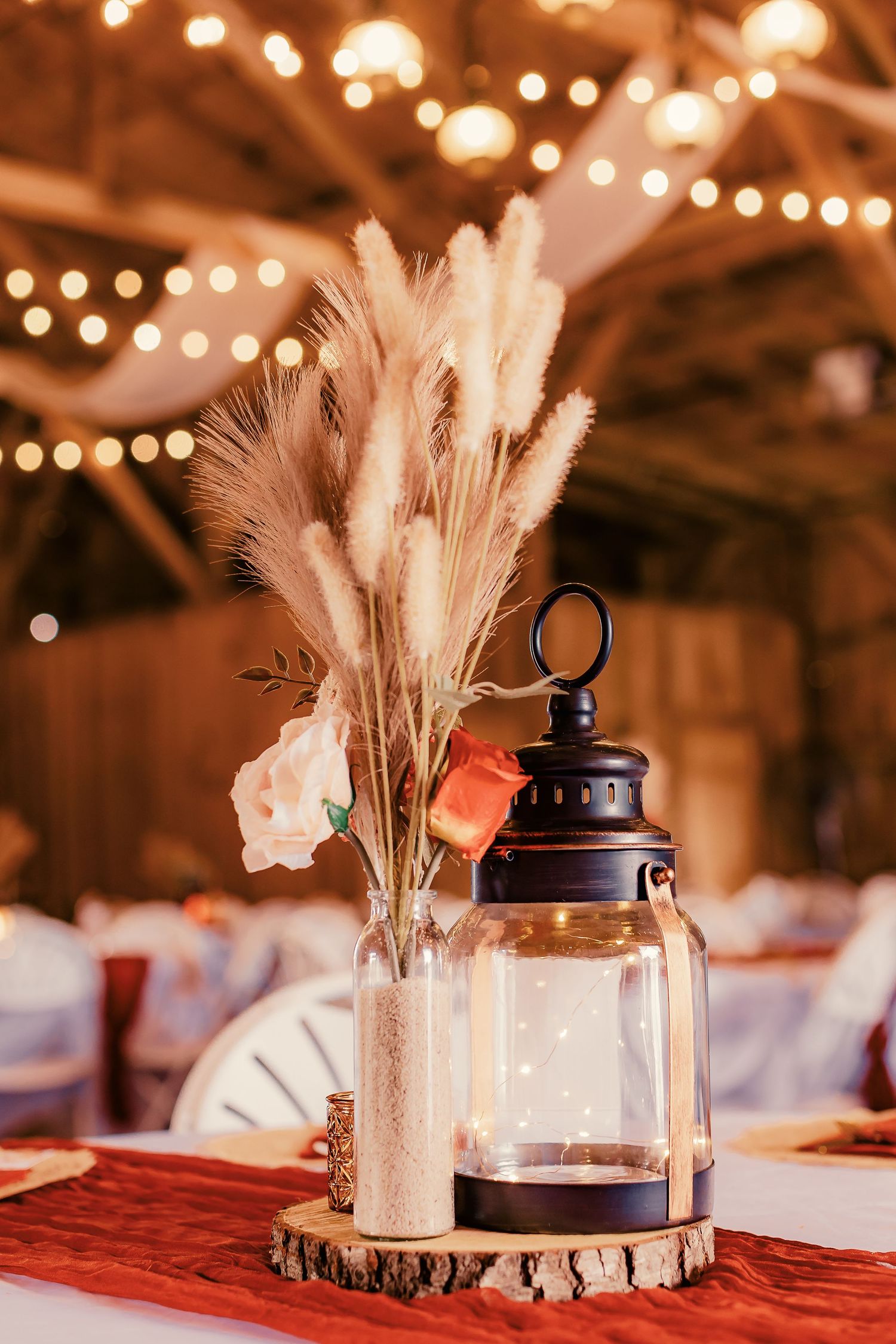 Wedding reception table decor with pampas grass centerpieces and lanterns under string lights.