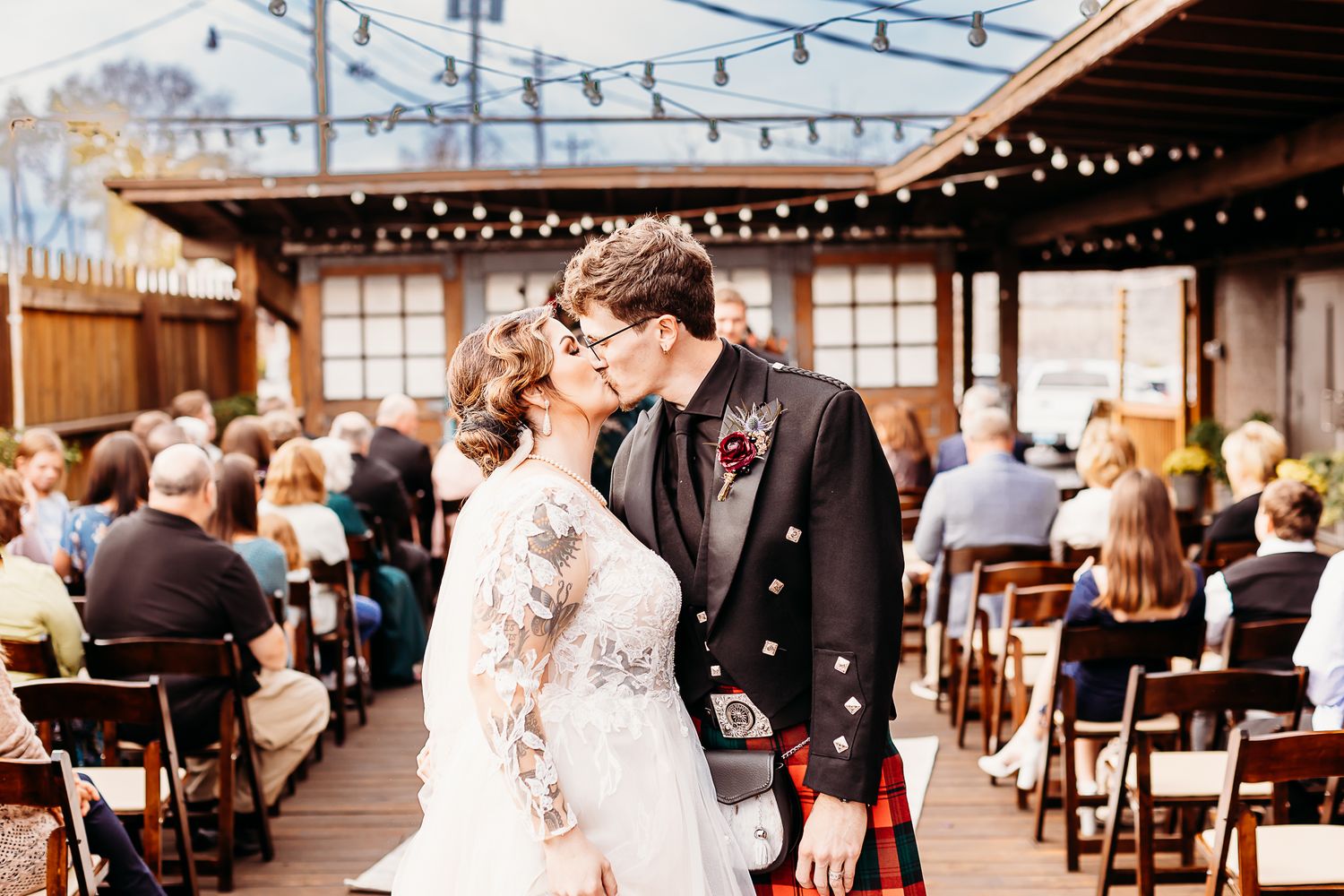 Wedding ceremony on outdoor deck with string lights and wooden chairs.