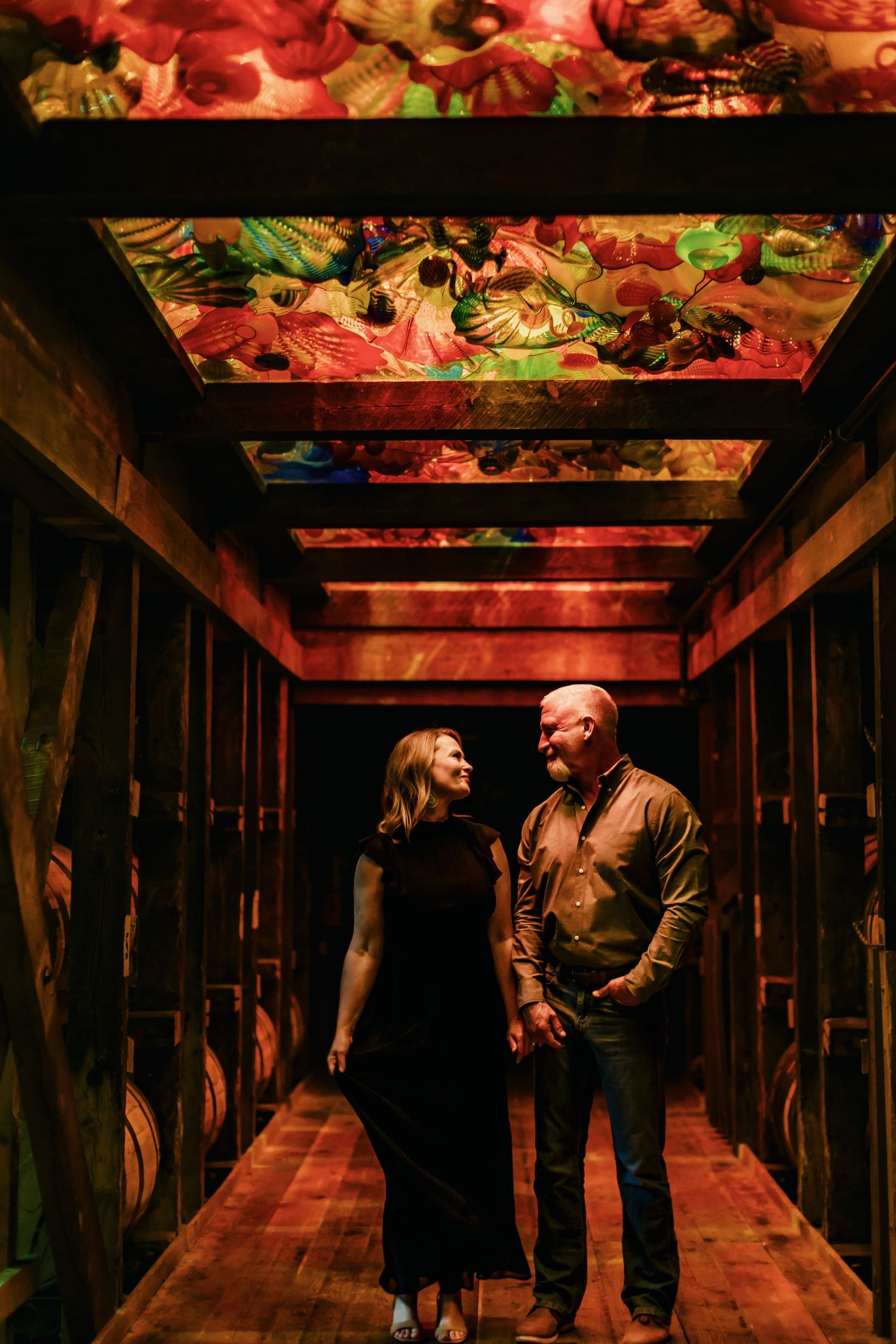Couple holding hands in a warmly lit corridor with vibrant colorful glass ceiling art at Chihuly Garden and Glass.