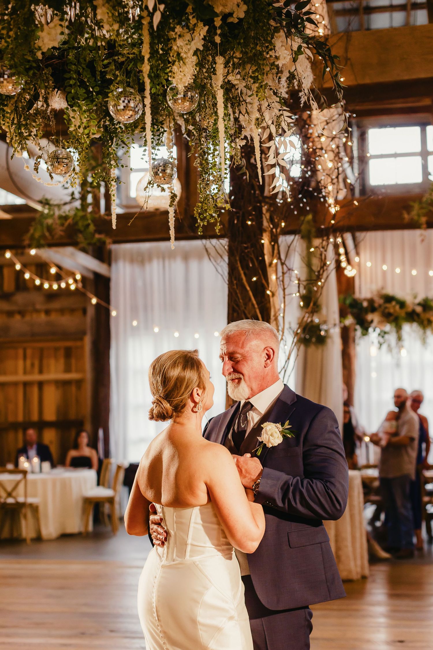 A romantic dance sequence at a rustic barn wedding venue decorated with hanging greenery and string lights.