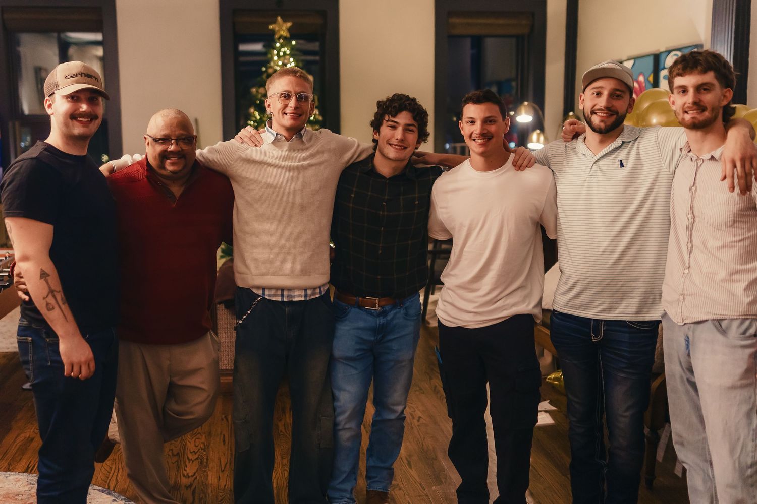 A group of friends posing together for a photo at a holiday gathering with a Christmas tree in background.