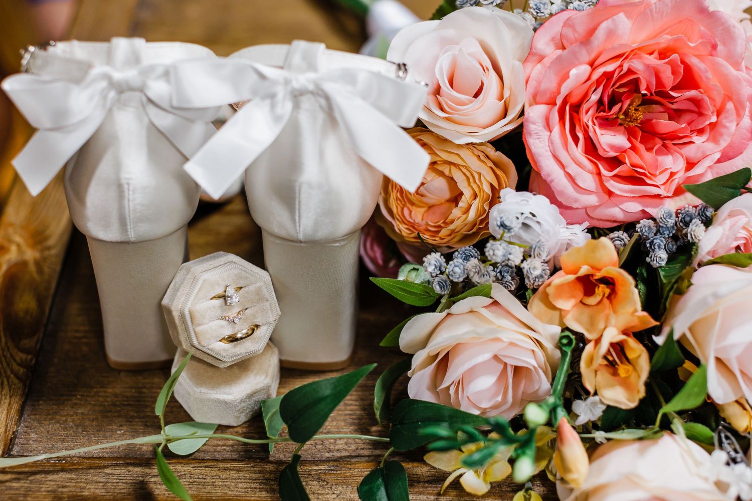 Elegant wedding favors and decor featuring peach and coral roses with white ribbons arranged on rustic wooden surface.