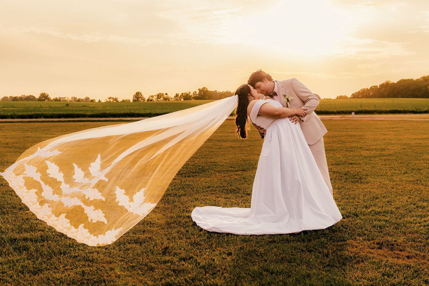 Flowing lace veil catching golden sunlight in an open field during sunset.