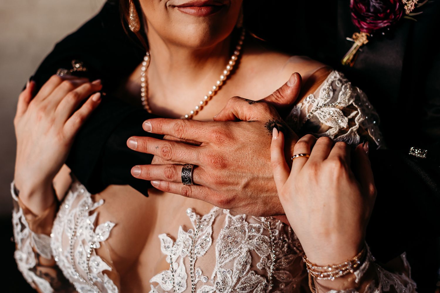 Close up detail of wedding jewelry and lace dress bodice with pearl necklace and ring.