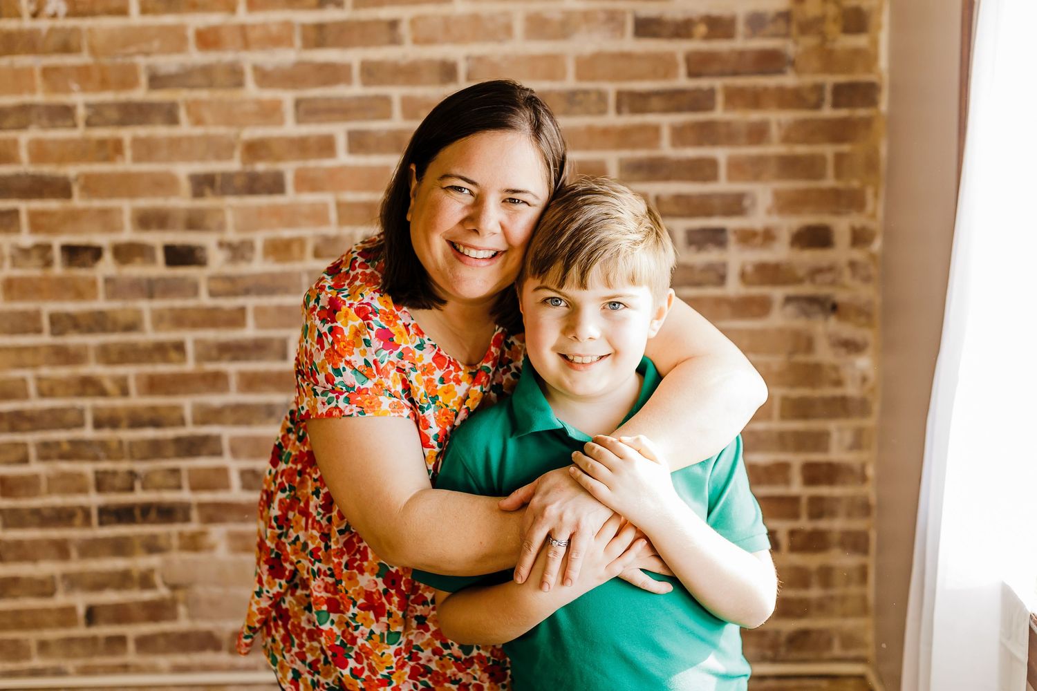Warm embrace captured against exposed brick wall during indoor photoshoot.