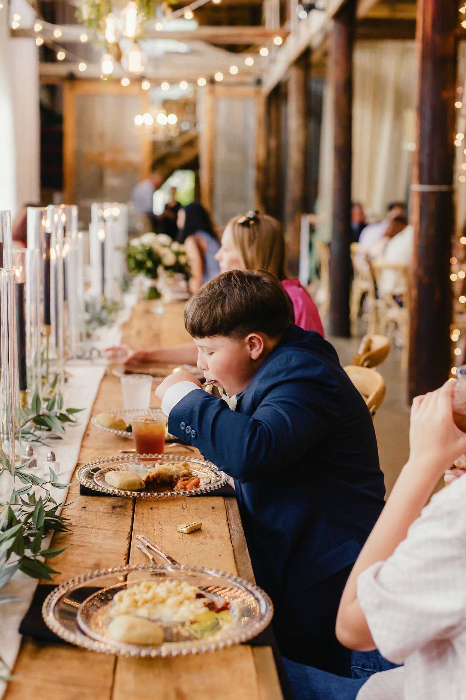Long wooden dining tables set with elegant place settings and greenery for a rustic wedding reception.