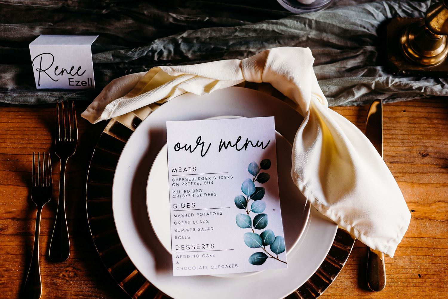 Wedding reception place setting with menu card featuring eucalyptus design and cream napkin.