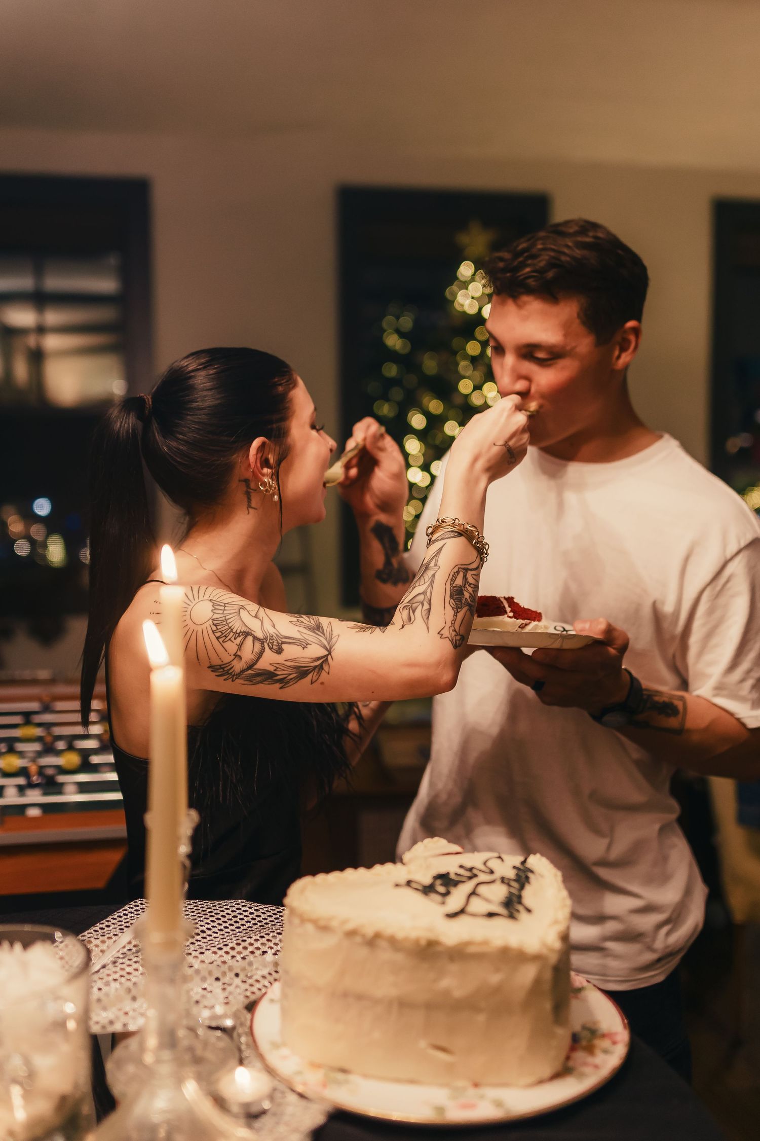 A couple sharing cake at a festive celebration with a decorated white cake on display.