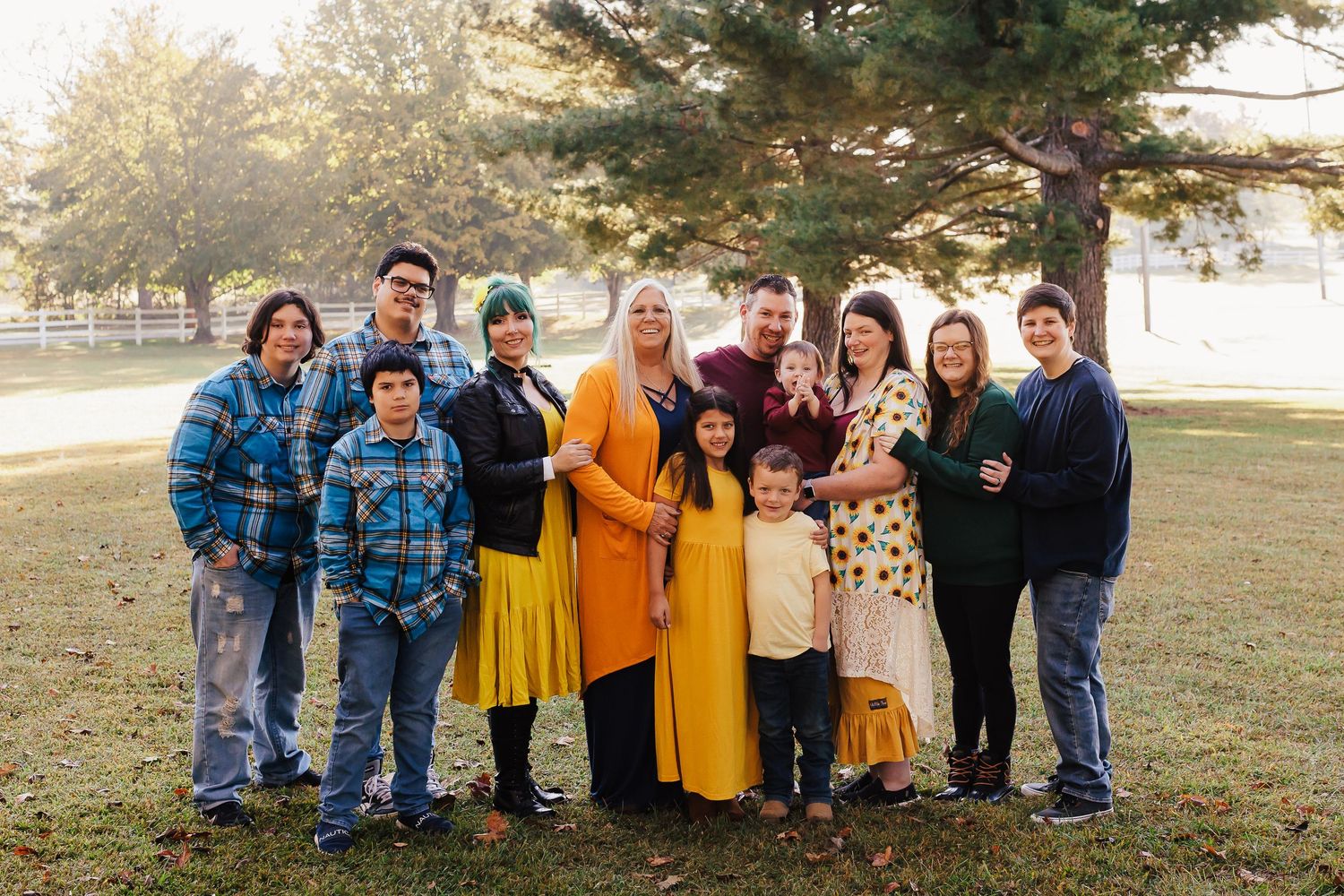 Large group photo of friends and family gathered outdoors under pine trees.