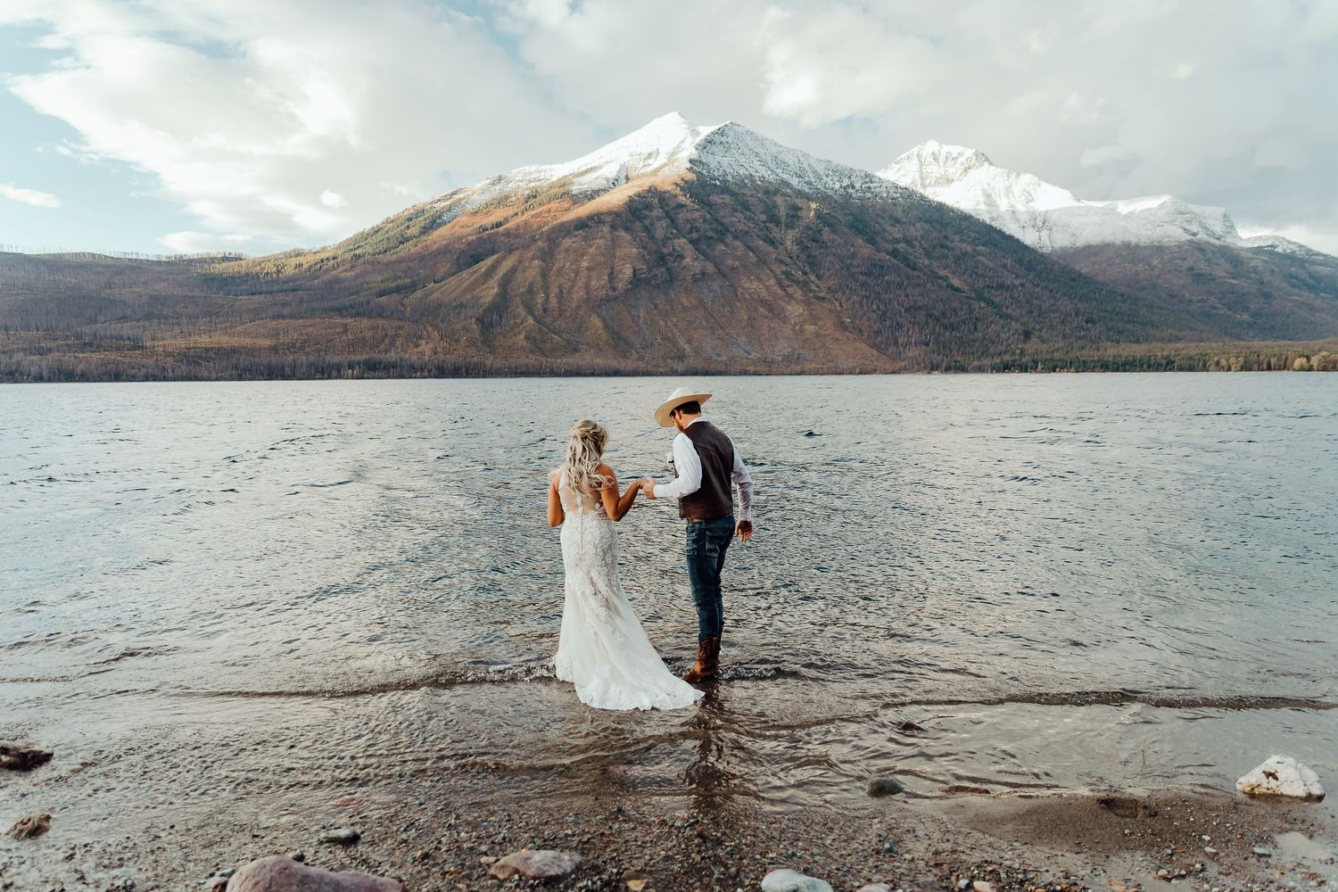 A couple poses together along a scenic mountain lake shore during an outdoor photo session.