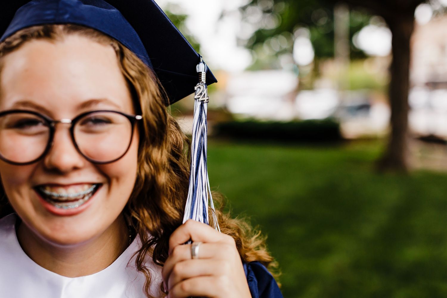A graduate in cap and gown holds their tassel while smiling outdoors.