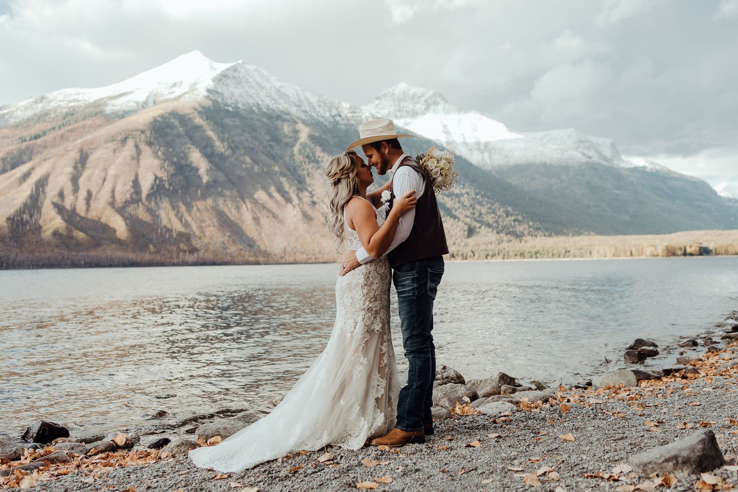 A romantic wedding ceremony on a rocky beach with snow-capped mountains in the background.