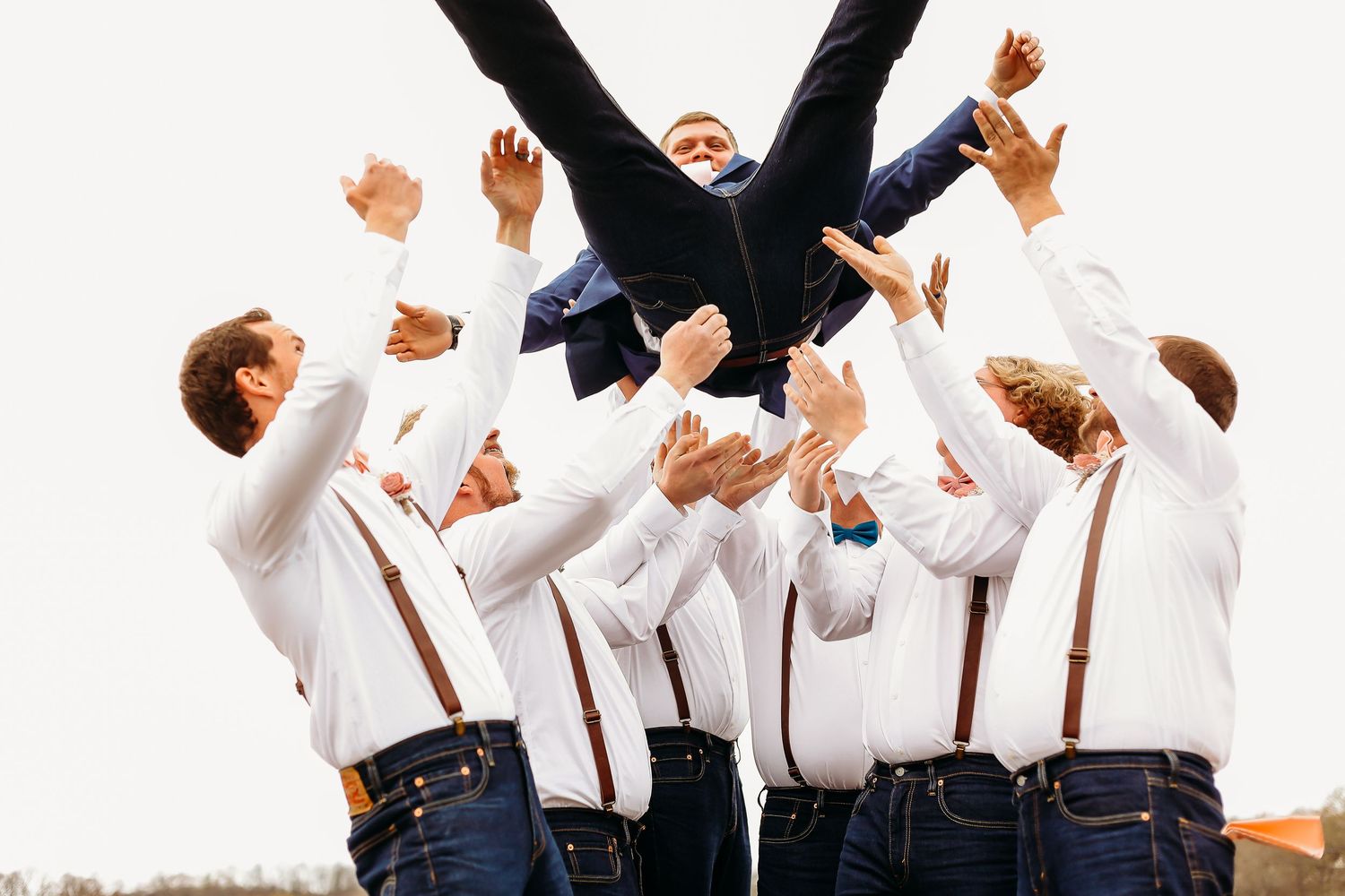 Groomsmen jumping in celebration wearing suspenders and white shirts.