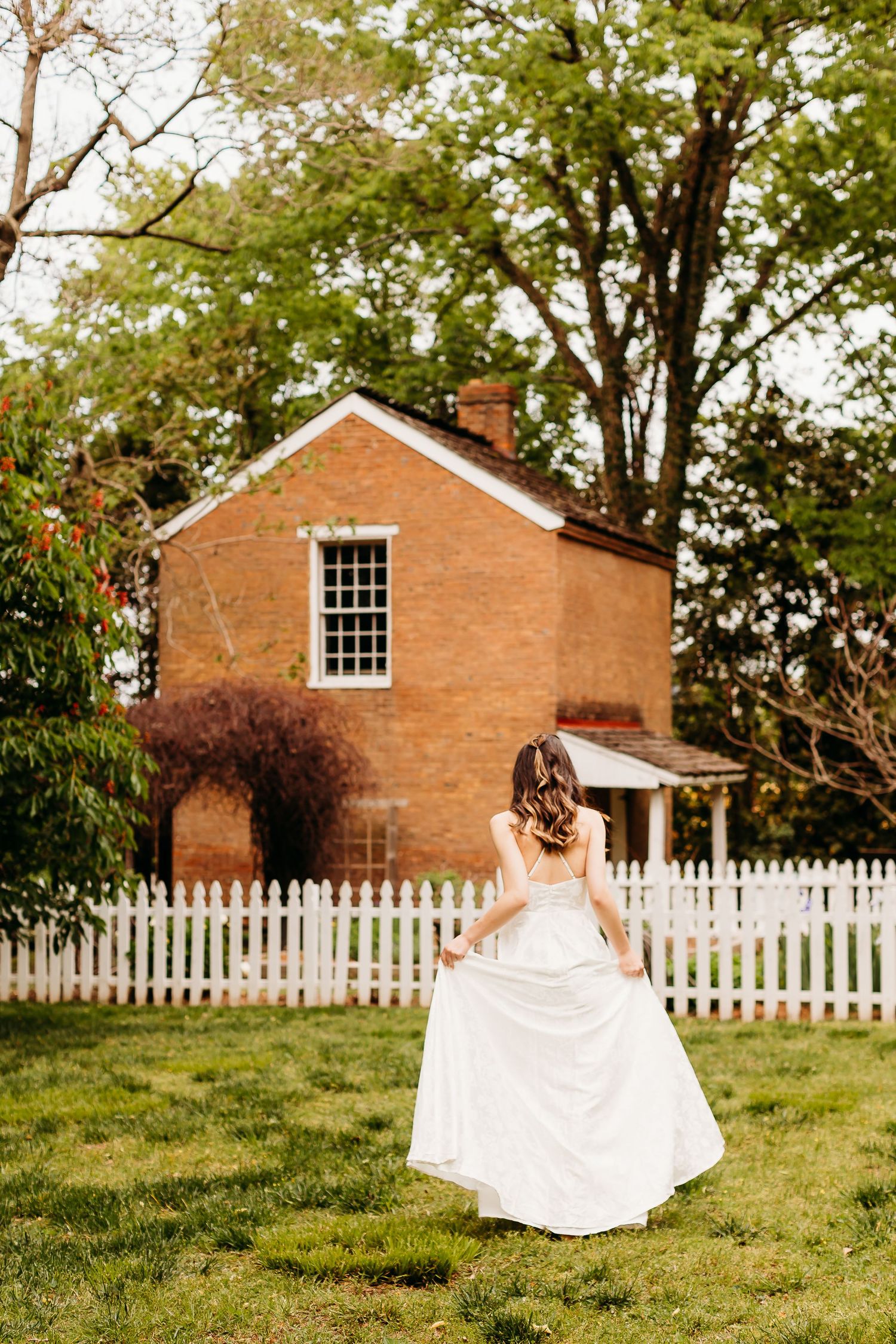 White wedding dress twirling in front of a brick house with white picket fence.