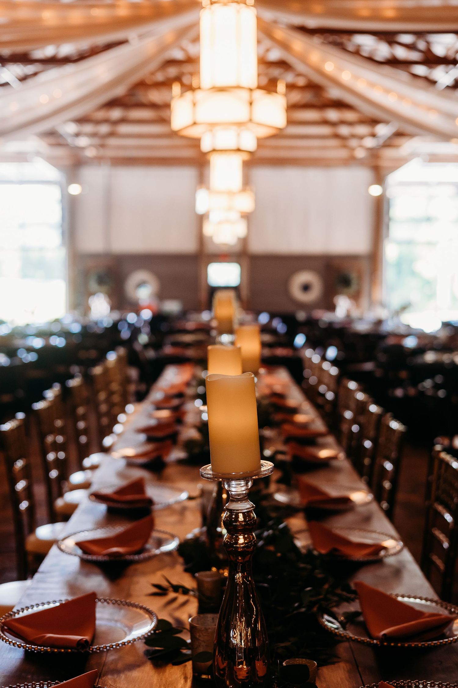 Wedding reception tables set with burgundy napkins and elegant place settings under warm lighting.
