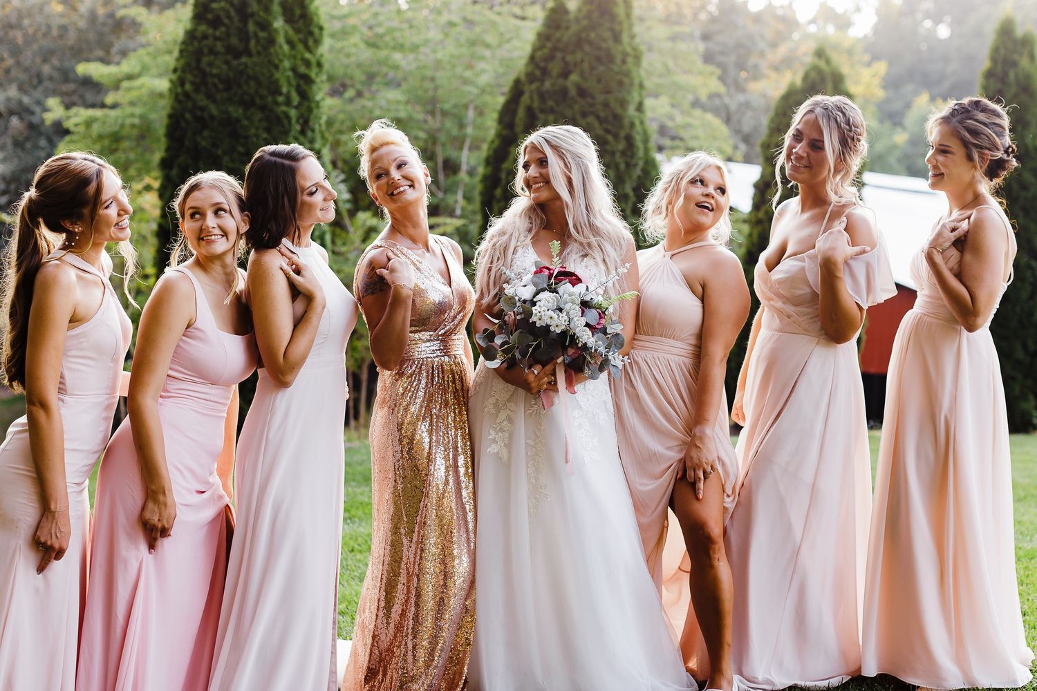 Bridesmaids lineup wearing blush pink and sparkly dresses in an outdoor garden setting.
