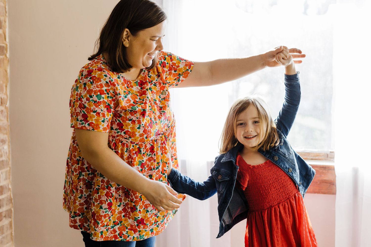 Two people dancing joyfully together in a sunlit room with brick walls.
