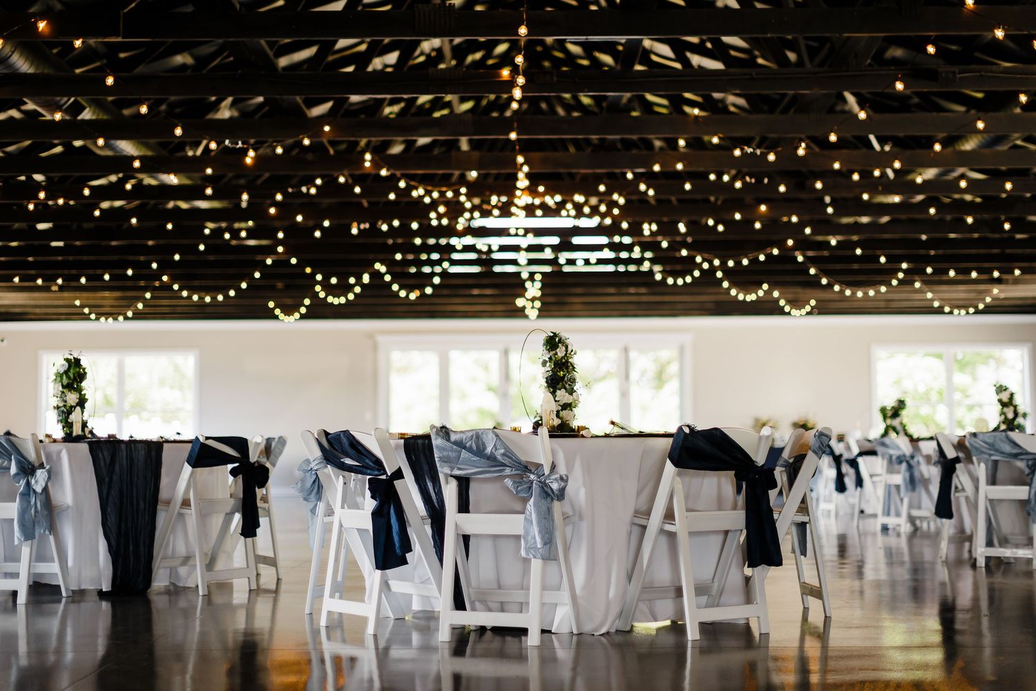 An elegant wedding reception setup with white chairs and twinkling lights overhead.